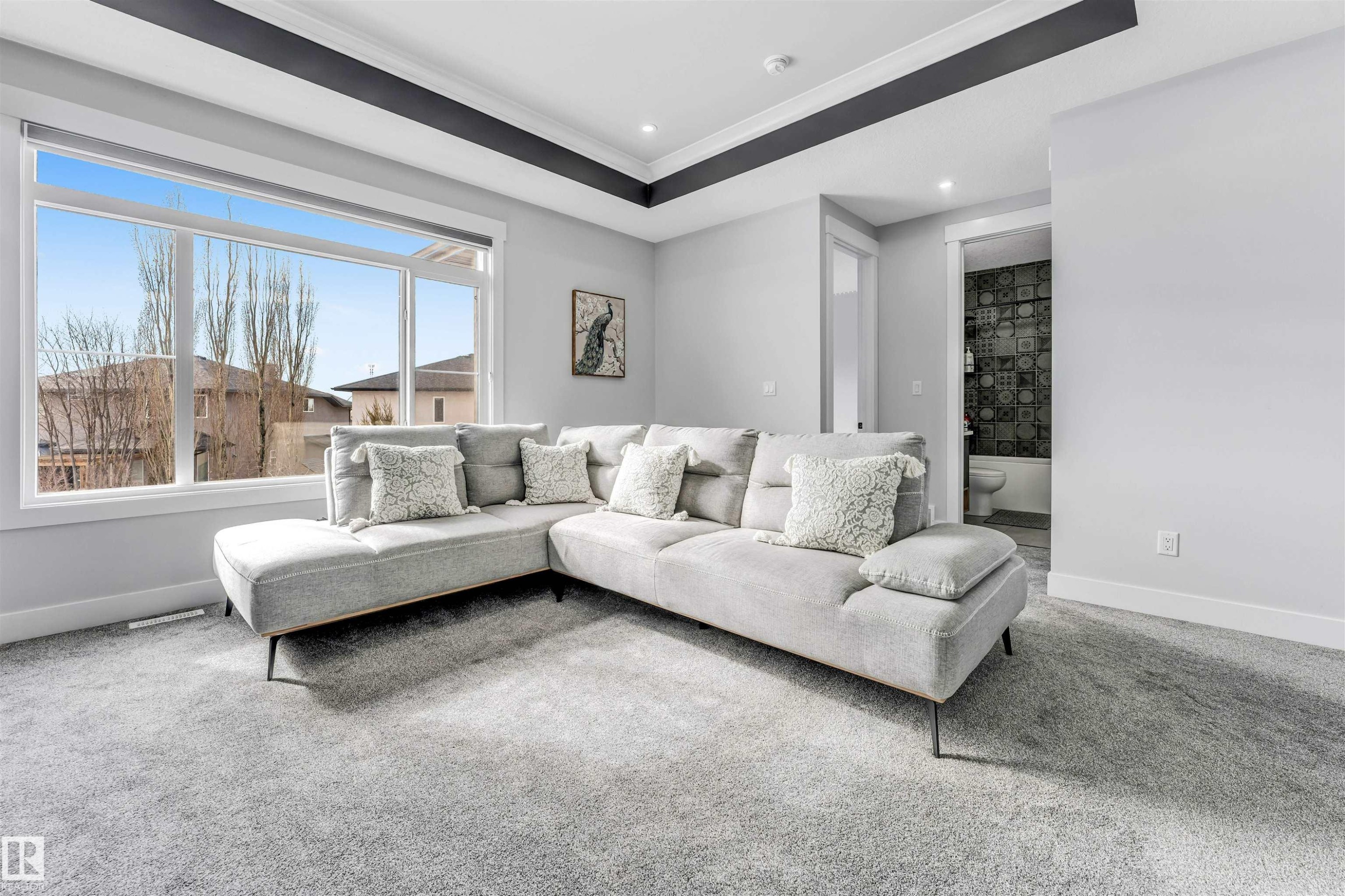 This living space features a large window with views of the surrounding neighborhood, light grey carpeting, and a tray ceiling with dark trim - 1531 151 Avenue, Edmonton, AB - Indoor Photo Showing Living Room