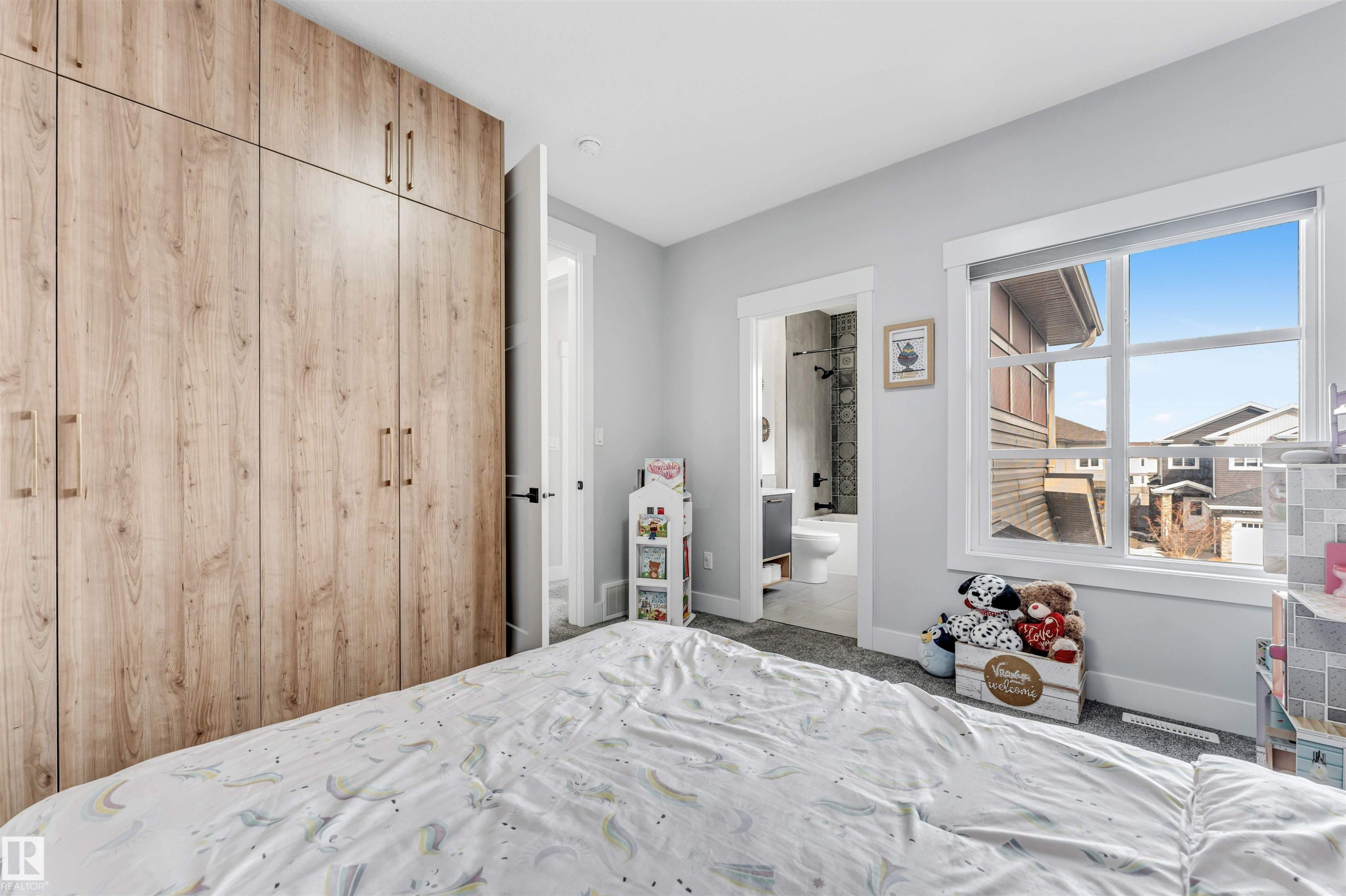This room features light wood-grain cabinetry with modern handles, a large window offering natural light, and plush carpet flooring - 1531 151 Avenue, Edmonton, AB - Indoor Photo Showing Bedroom