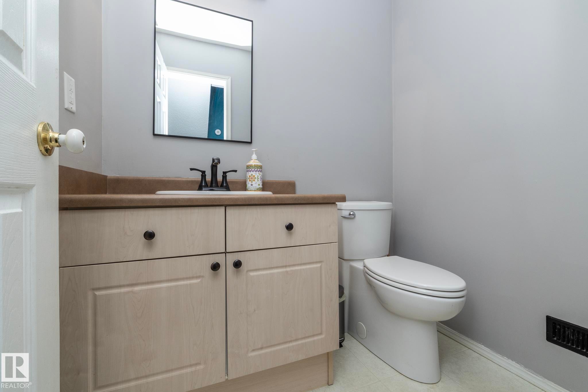 The bathroom features a light-colored vanity with black hardware, a rectangular mirror, a black faucet, and a toilet - 6 Glaewyn Estates, St. Albert, AB - Indoor Photo Showing Bathroom