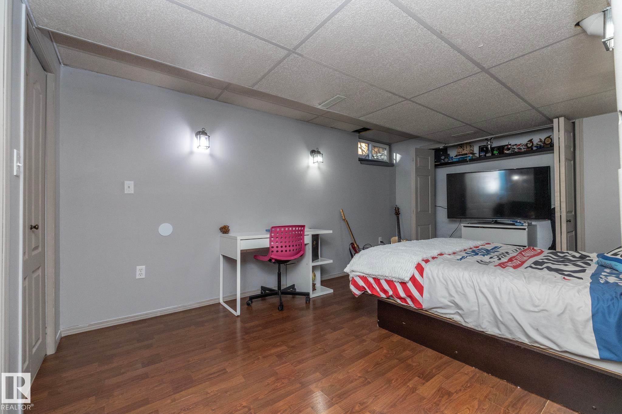 A bedroom space featuring light gray walls, warm-toned wood flooring, and a drop ceiling - 6 Glaewyn Estates, St. Albert, AB - Indoor Photo Showing Bedroom