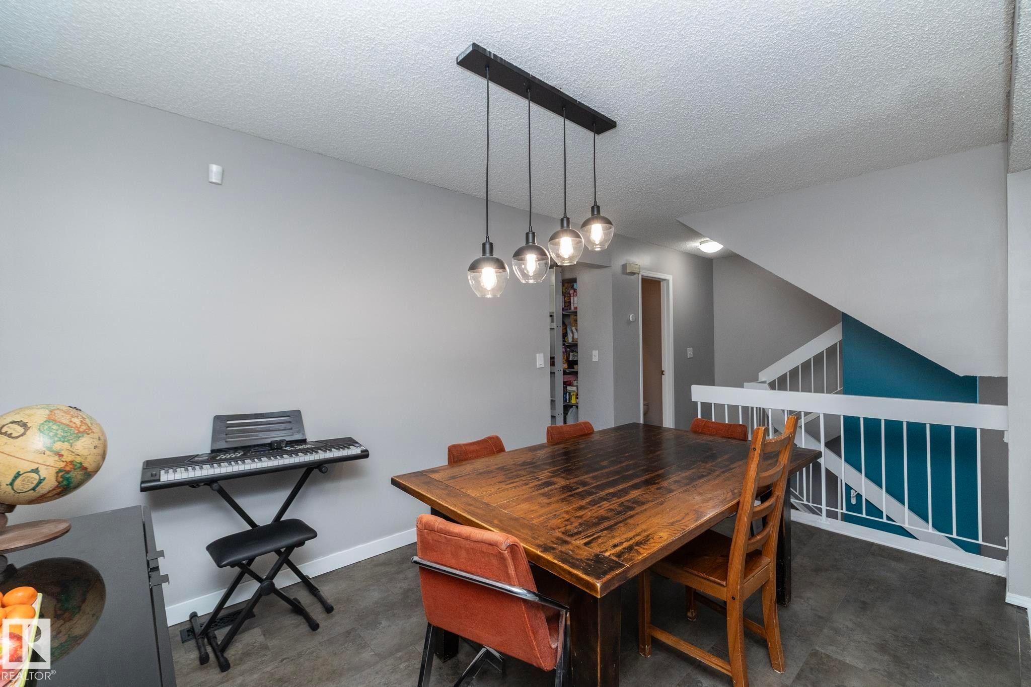 The dining area features a modern linear pendant light fixture with four spherical bulbs, providing illumination over a rustic wooden dining table - 6 Glaewyn Estates, St. Albert, AB - Indoor
