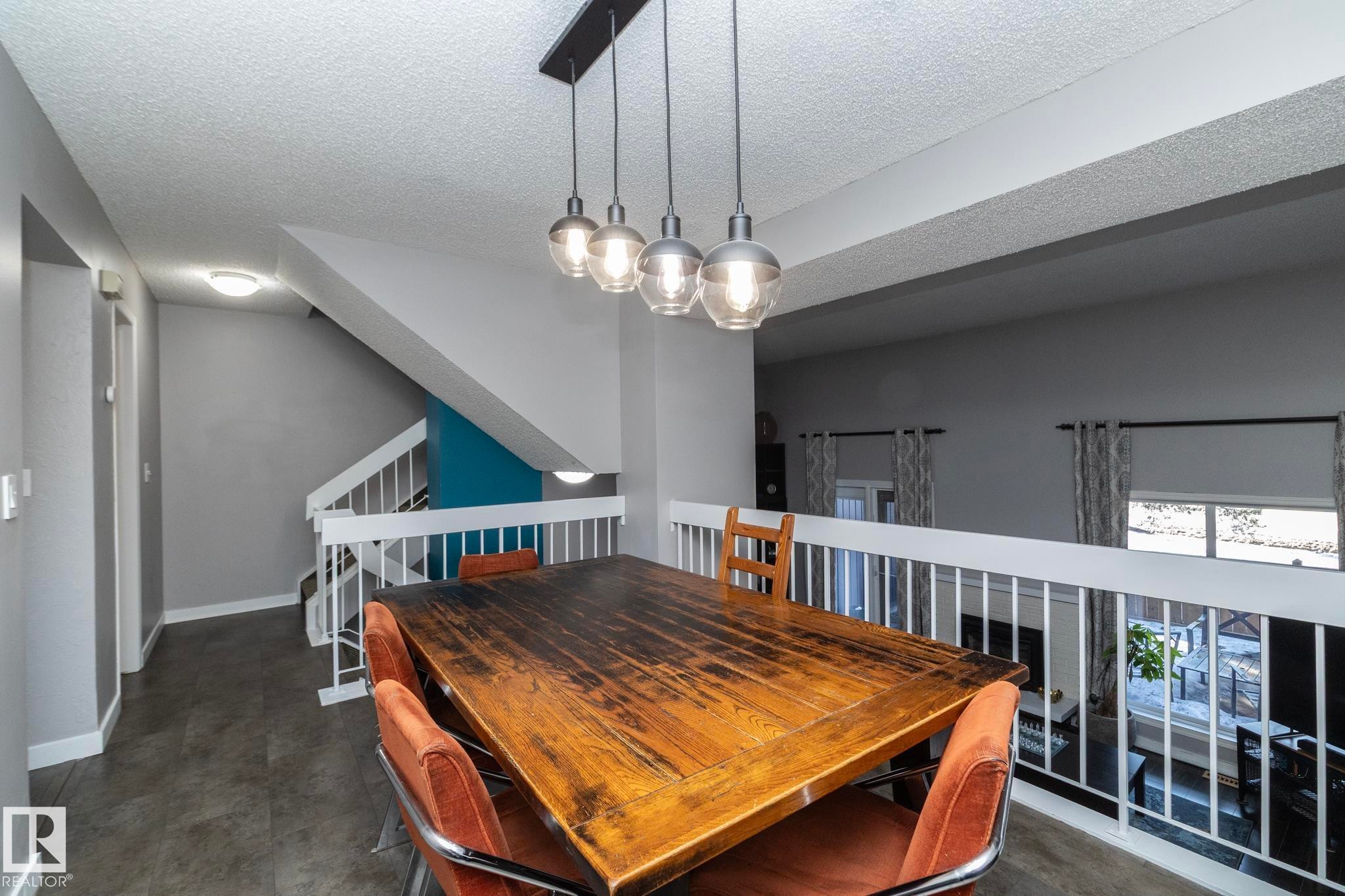 The property features a dining area with a rustic wooden table and a contemporary four-light pendant fixture overhead - 6 Glaewyn Estates, St. Albert, AB - Indoor Photo Showing Dining Room