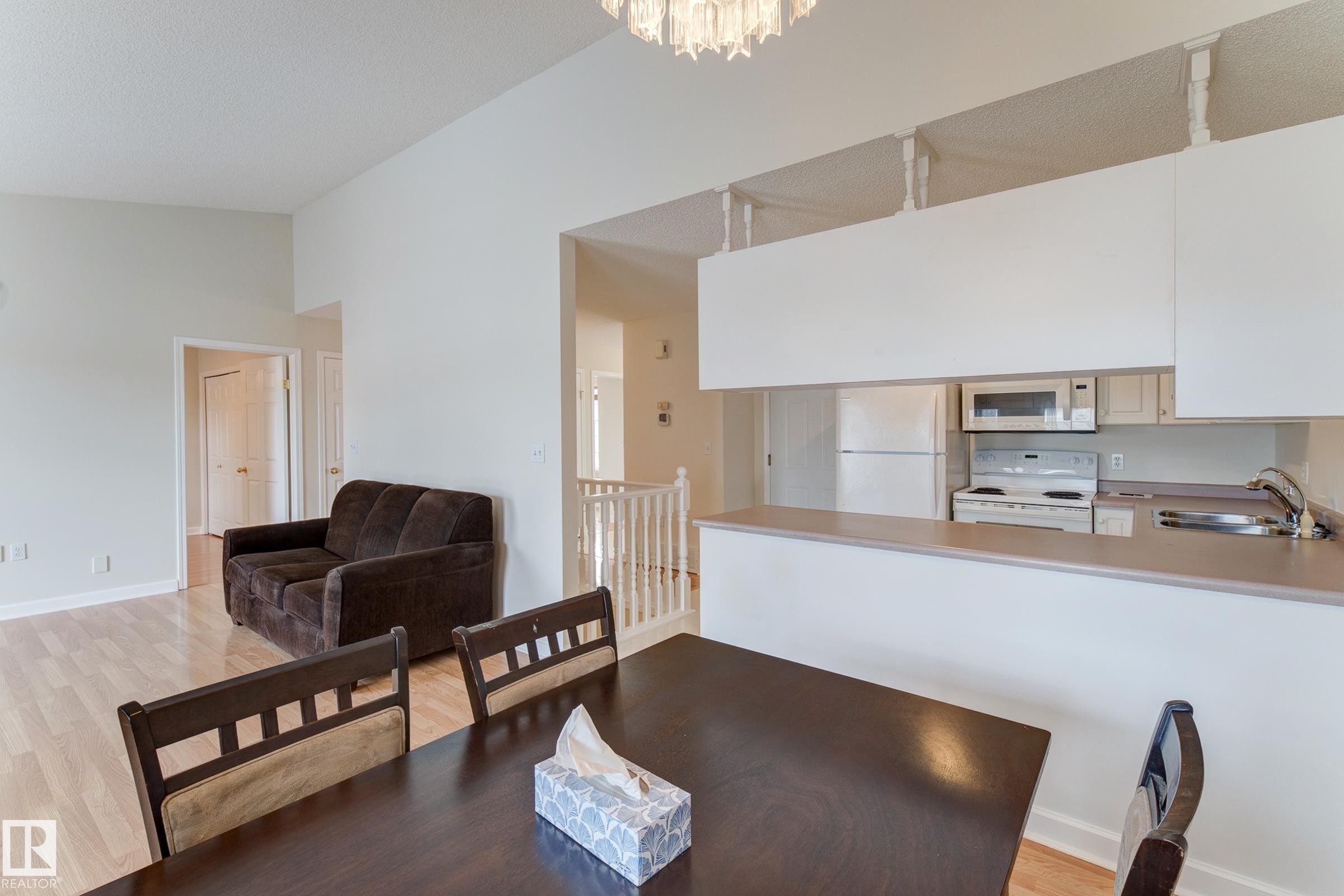 The open concept living area features light-toned flooring, a kitchen with white appliances and cabinets, and a breakfast bar with a light countertop - 5 308 Jackson Road, Edmonton, AB - Indoor Photo Showing Kitchen With Double Sink