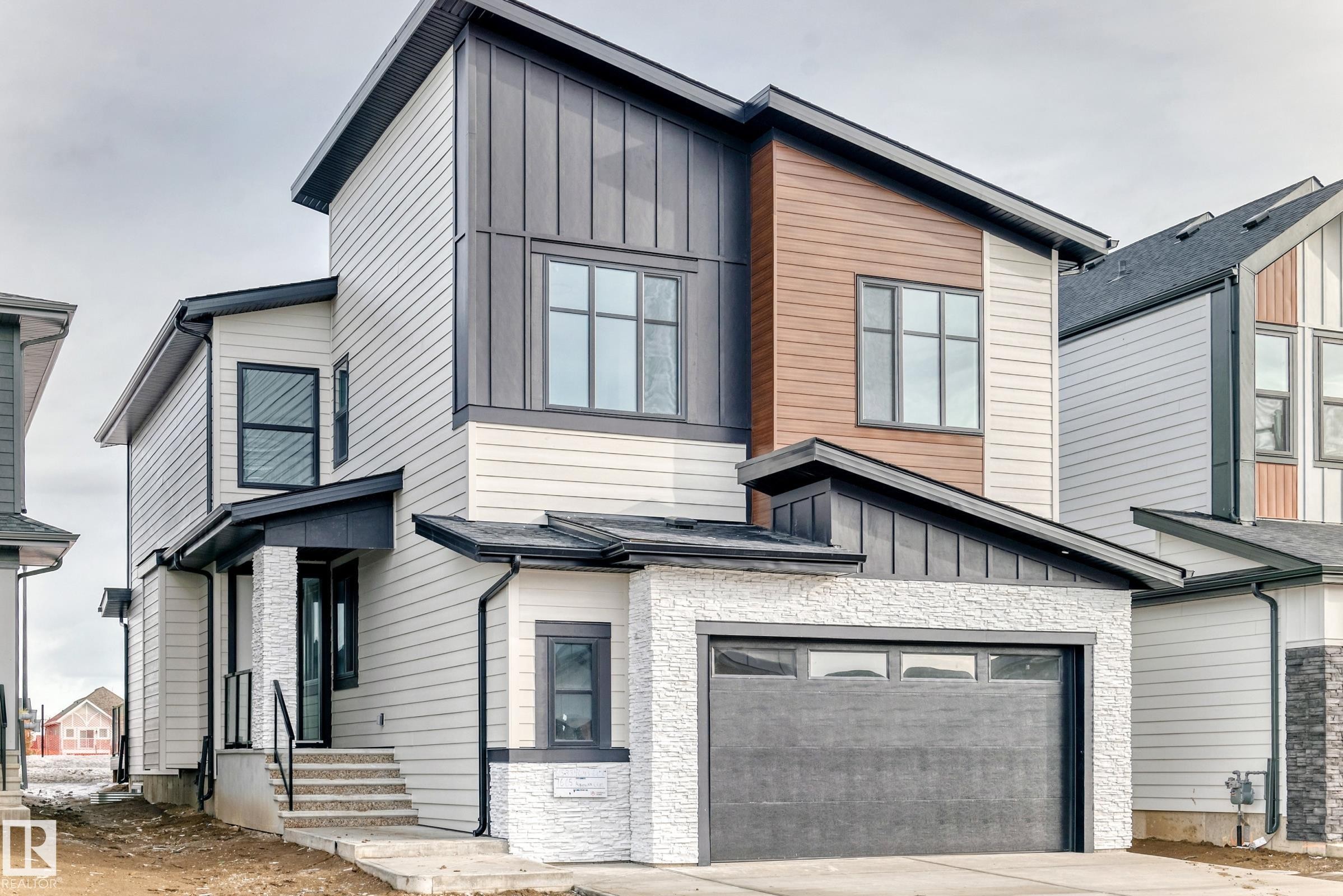 The property features a contemporary exterior with light-colored siding, dark trim, and a prominent attached garage - 7665 Kimiwan Crescent, Edmonton, AB - Outdoor