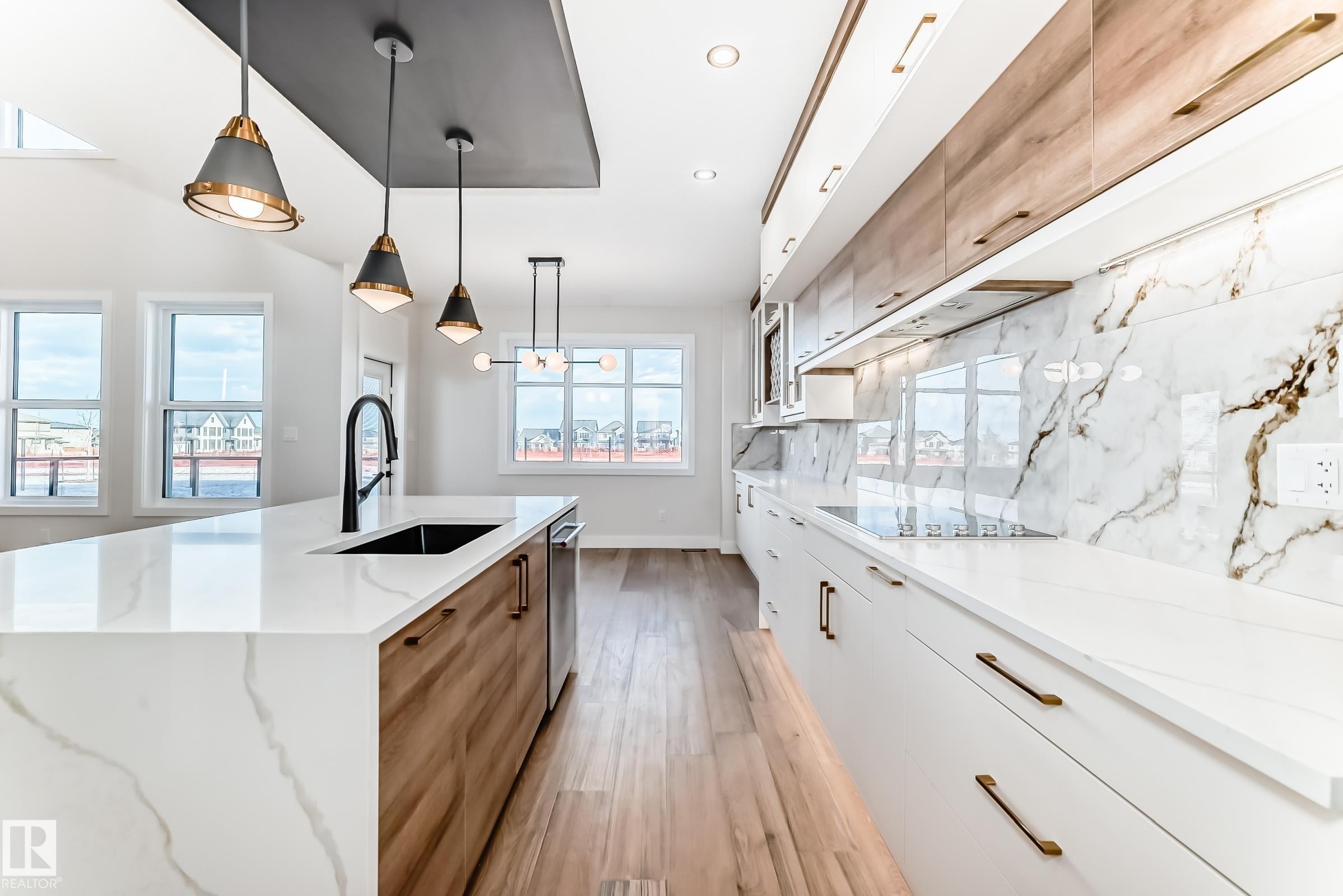 The kitchen features a spacious island with a built-in sink and pendant lighting, complemented by light wood flooring - 7665 Kimiwan Crescent, Edmonton, AB - Indoor Photo Showing Kitchen With Upgraded Kitchen