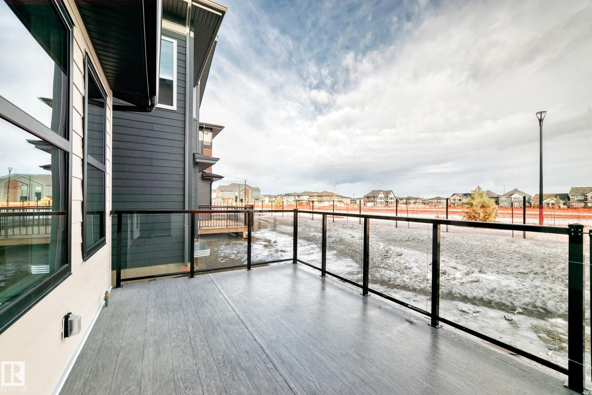 This property features a balcony with a glass railing and a wood-look floor, offering views of distant residential properties - 7665 Kimiwan Crescent, Edmonton, AB - Outdoor