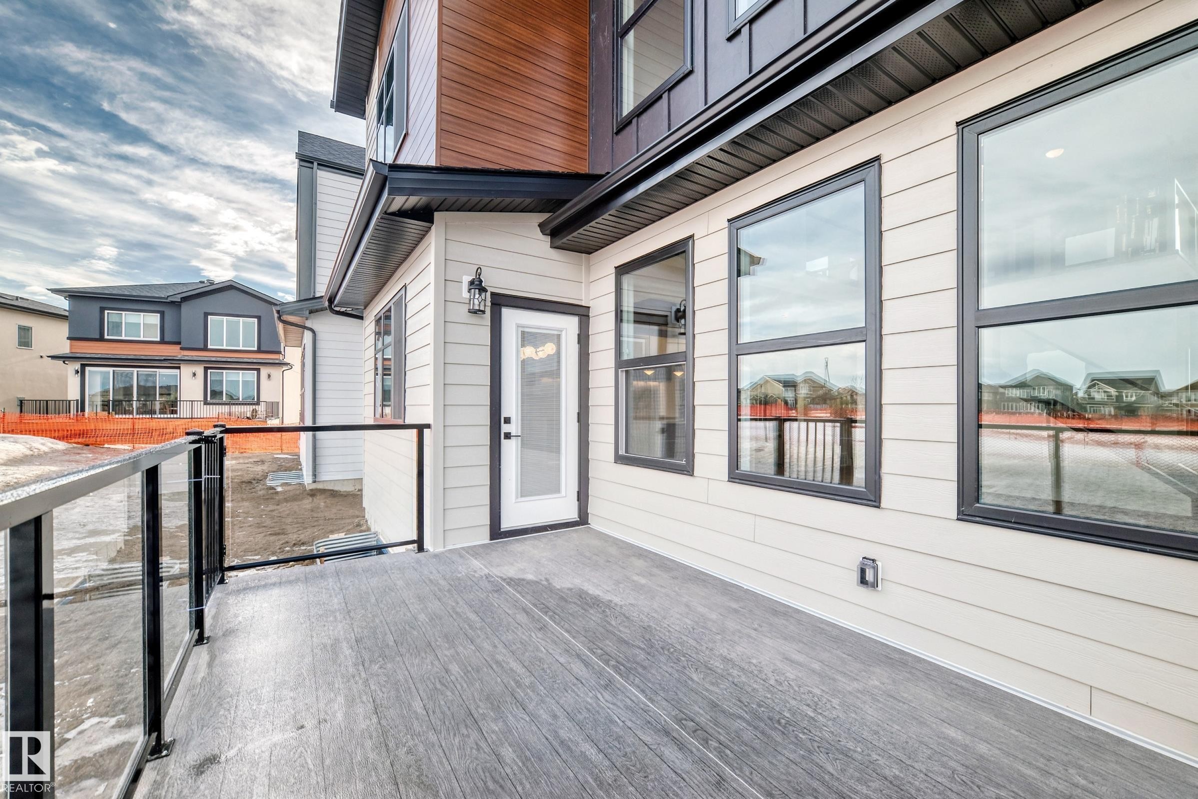 The property features a private deck with glass railings, a white exterior door, and large windows with black frames - 7665 Kimiwan Crescent, Edmonton, AB - Outdoor With Exterior