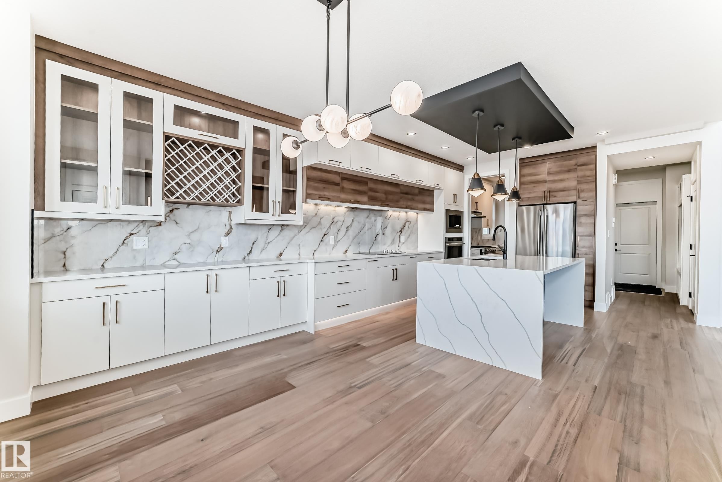 Modern kitchen featuring light hardwood flooring, an island with a waterfall countertop, and white cabinetry - 7665 Kimiwan Crescent, Edmonton, AB - Indoor Photo Showing Kitchen With Upgraded Kitchen