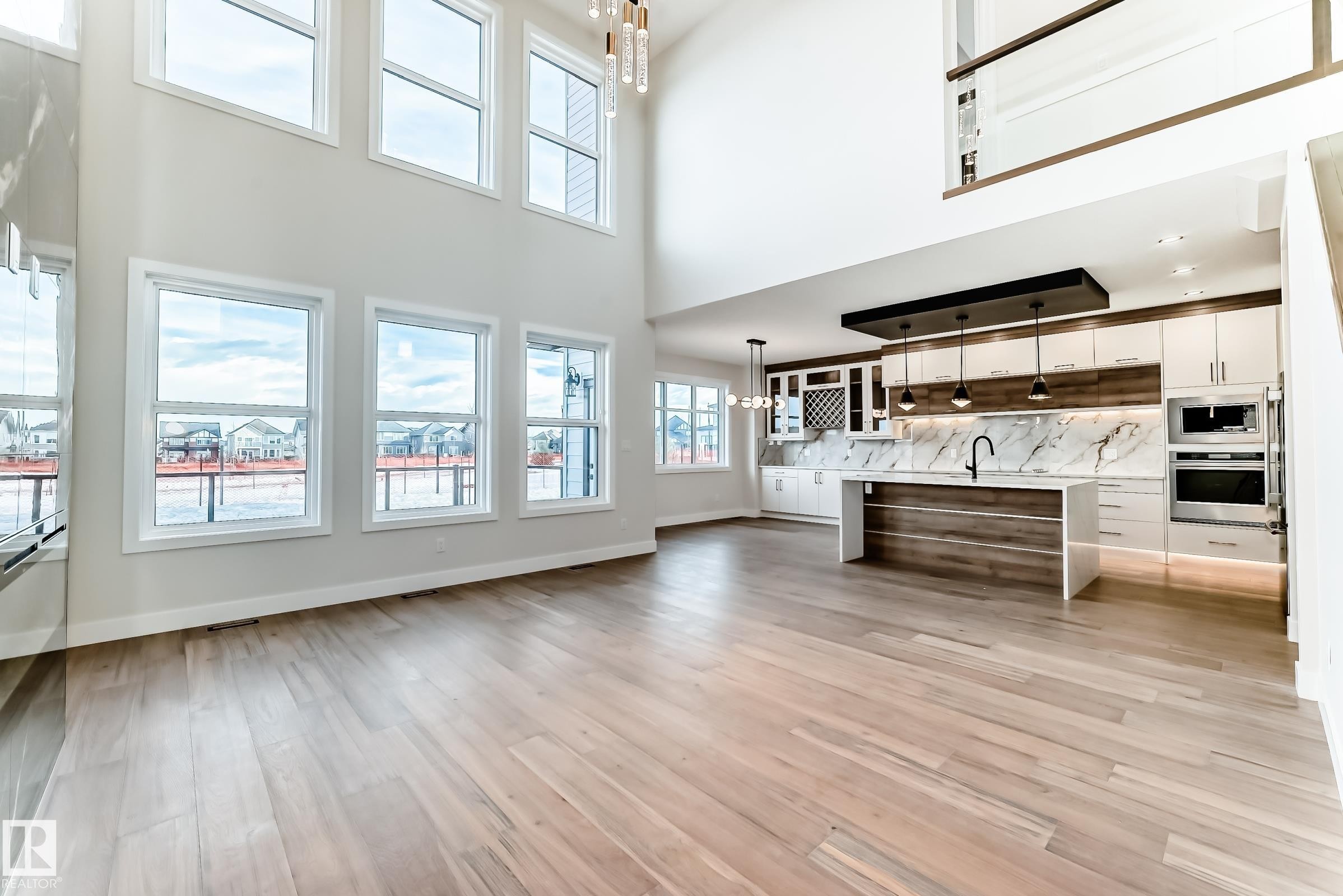 The open-concept living space features light wood flooring and high ceilings with large windows providing ample natural light - 7665 Kimiwan Crescent, Edmonton, AB - Indoor
