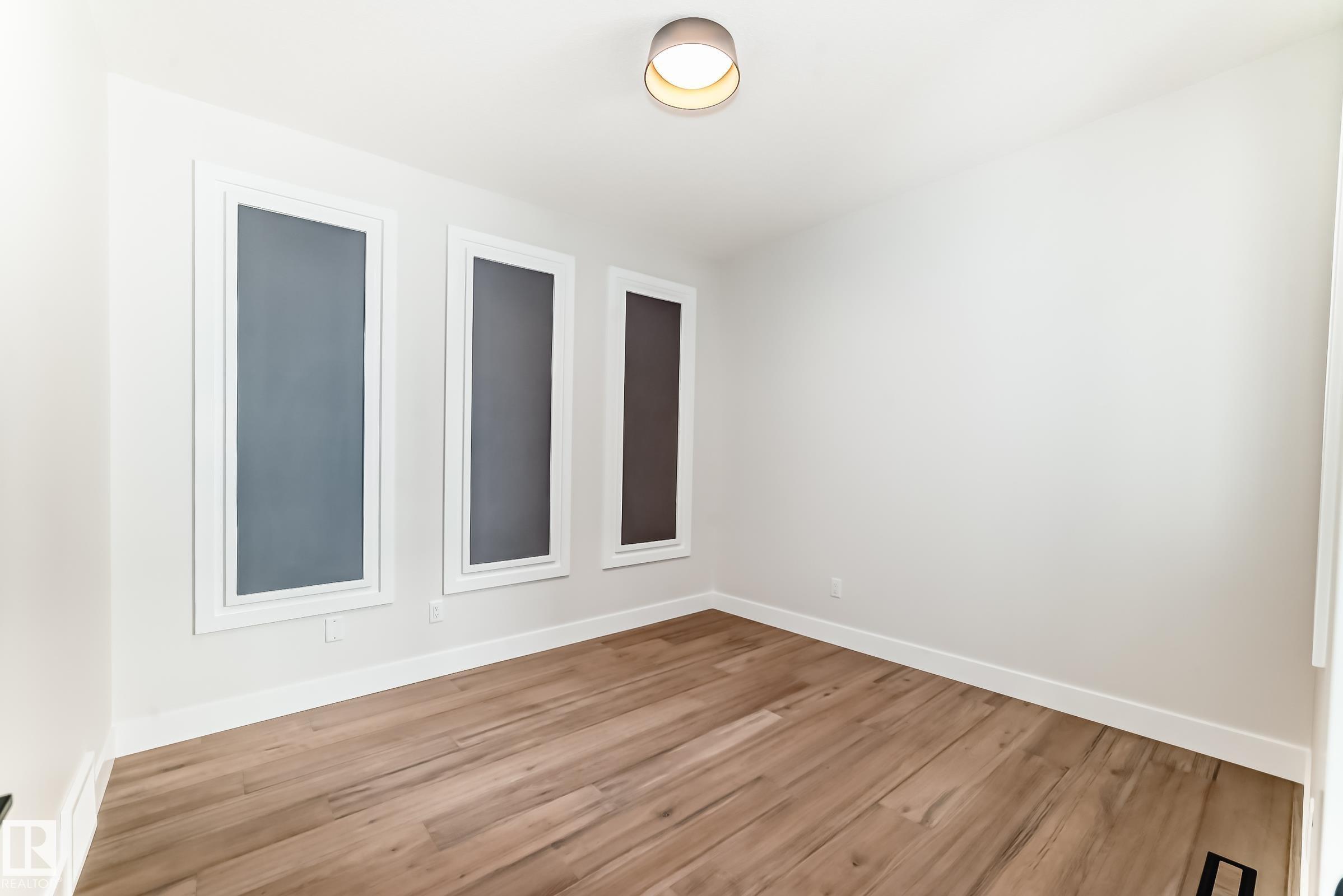 Interior space featuring light wood flooring, white walls, and three vertical windows - 7665 Kimiwan Crescent, Edmonton, AB - Indoor Photo Showing Other Room