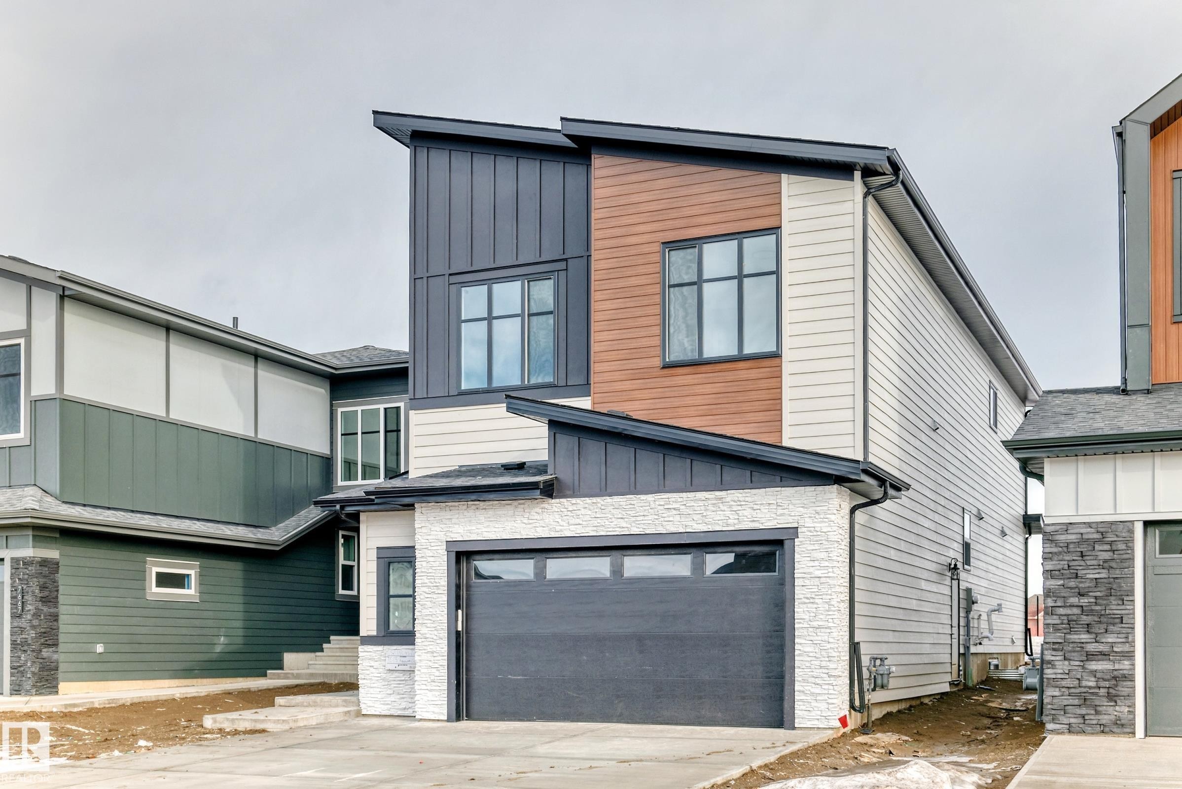 The property features a contemporary architectural style with varied siding materials, including light-colored horizontal siding, wood-toned vertical panels, and dark grey vertical siding - 7665 Kimiwan Crescent, Edmonton, AB - Outdoor With Exterior