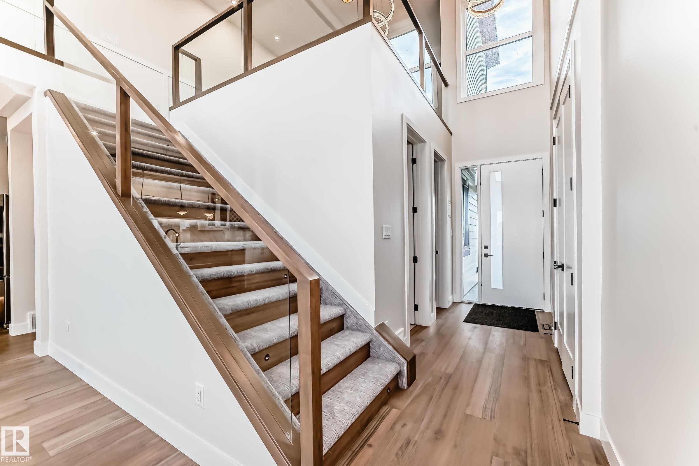 The property features a grand entryway with hardwood floors, a modern staircase with glass railings and carpeted treads, and a high ceiling with a large window above the front door - 7665 Kimiwan Crescent, Edmonton, AB - Indoor Photo Showing Other Room
