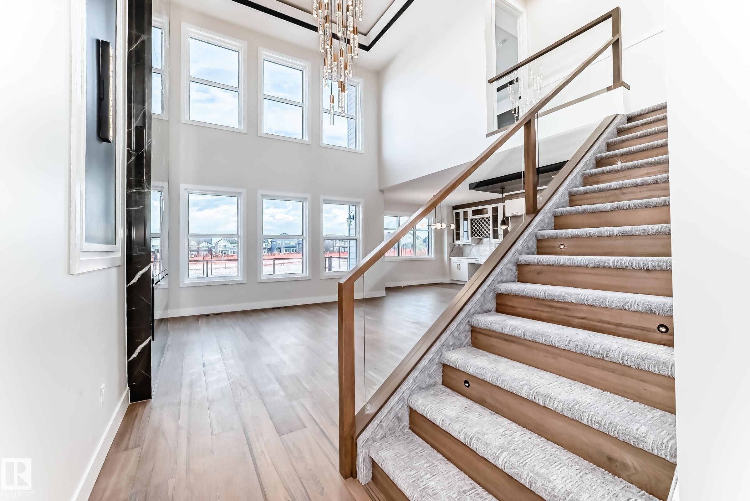 The property features a grand two-story living area with extensive windows providing abundant natural light, hardwood flooring, and a contemporary chandelier - 7665 Kimiwan Crescent, Edmonton, AB - Indoor Photo Showing Other Room