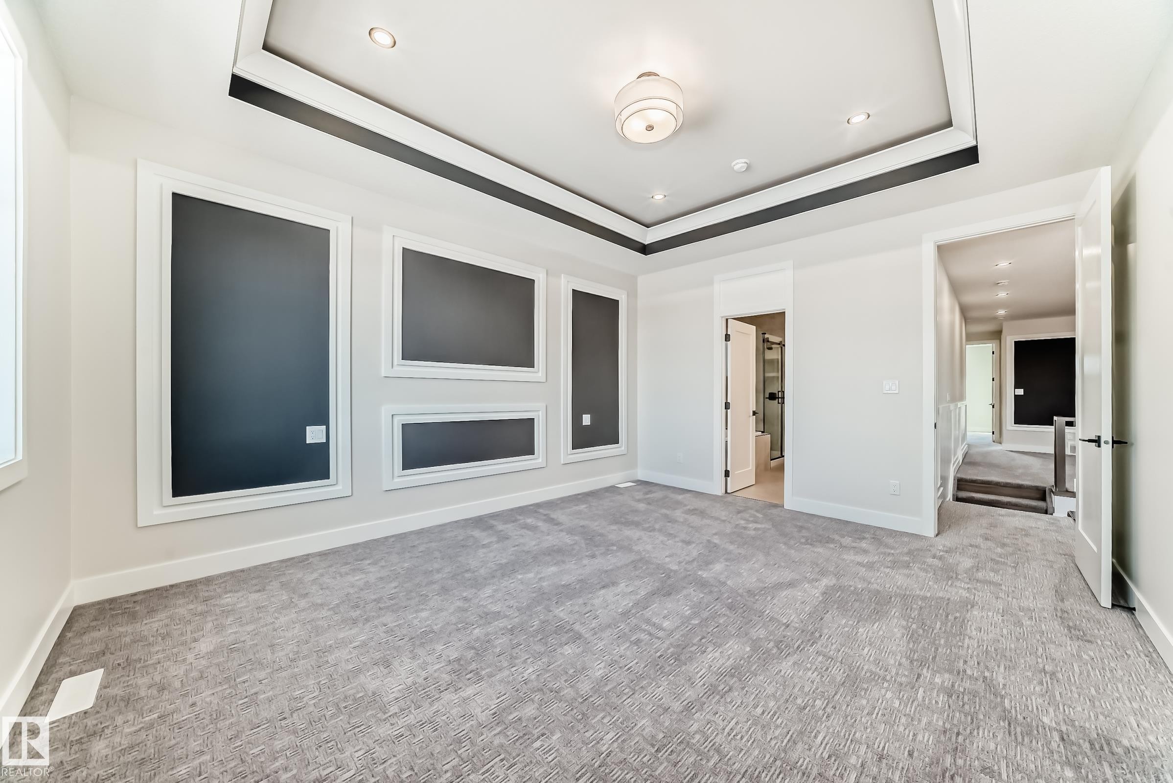 Expansive room featuring a tray ceiling with recessed lighting and a central light fixture, wall paneling with dark inserts, and plush grey carpeting - 7665 Kimiwan Crescent, Edmonton, AB - Indoor Photo Showing Other Room With Fireplace