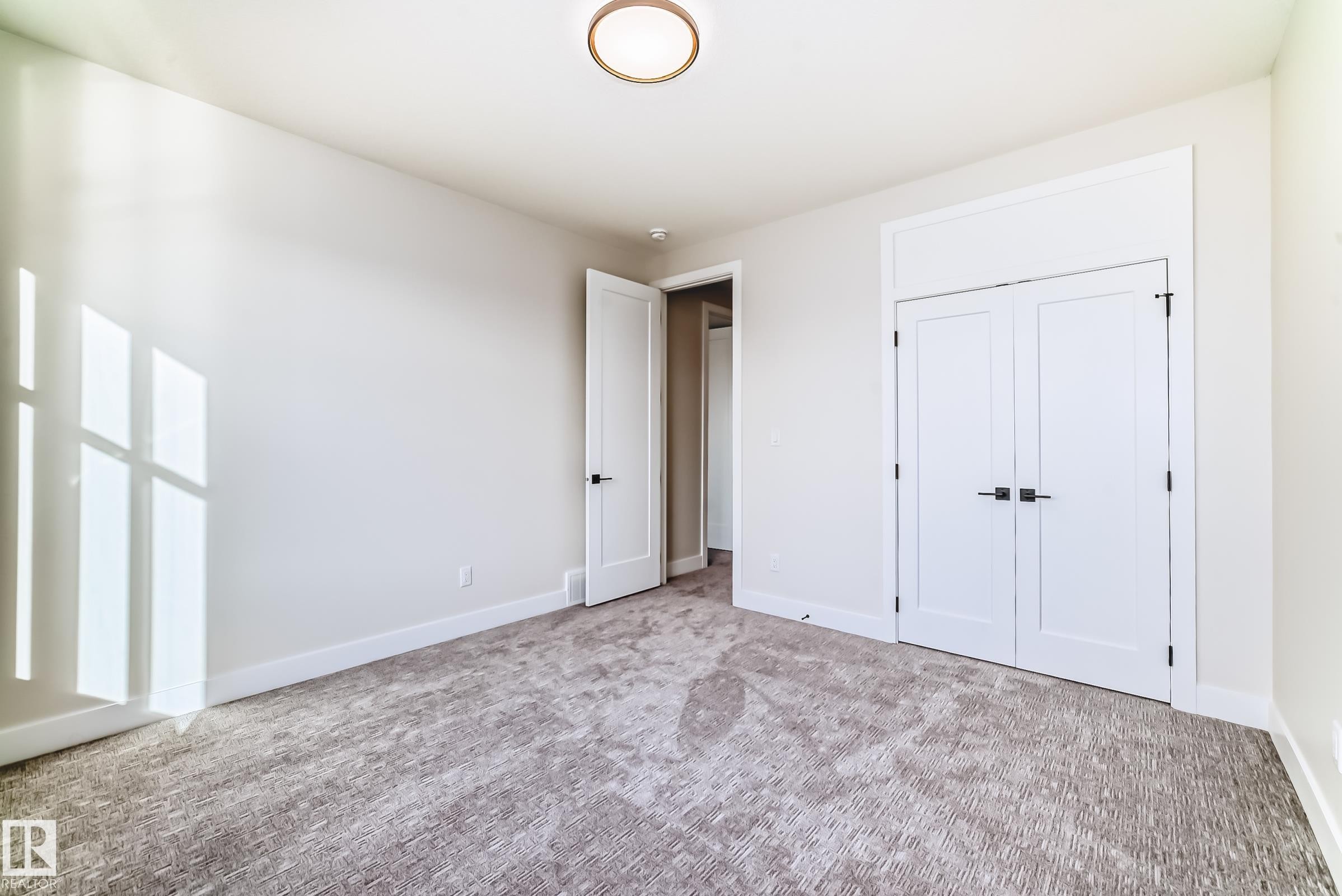Bright room featuring a ceiling light fixture, white walls, and light-colored patterned carpet - 7665 Kimiwan Crescent, Edmonton, AB - Indoor Photo Showing Other Room