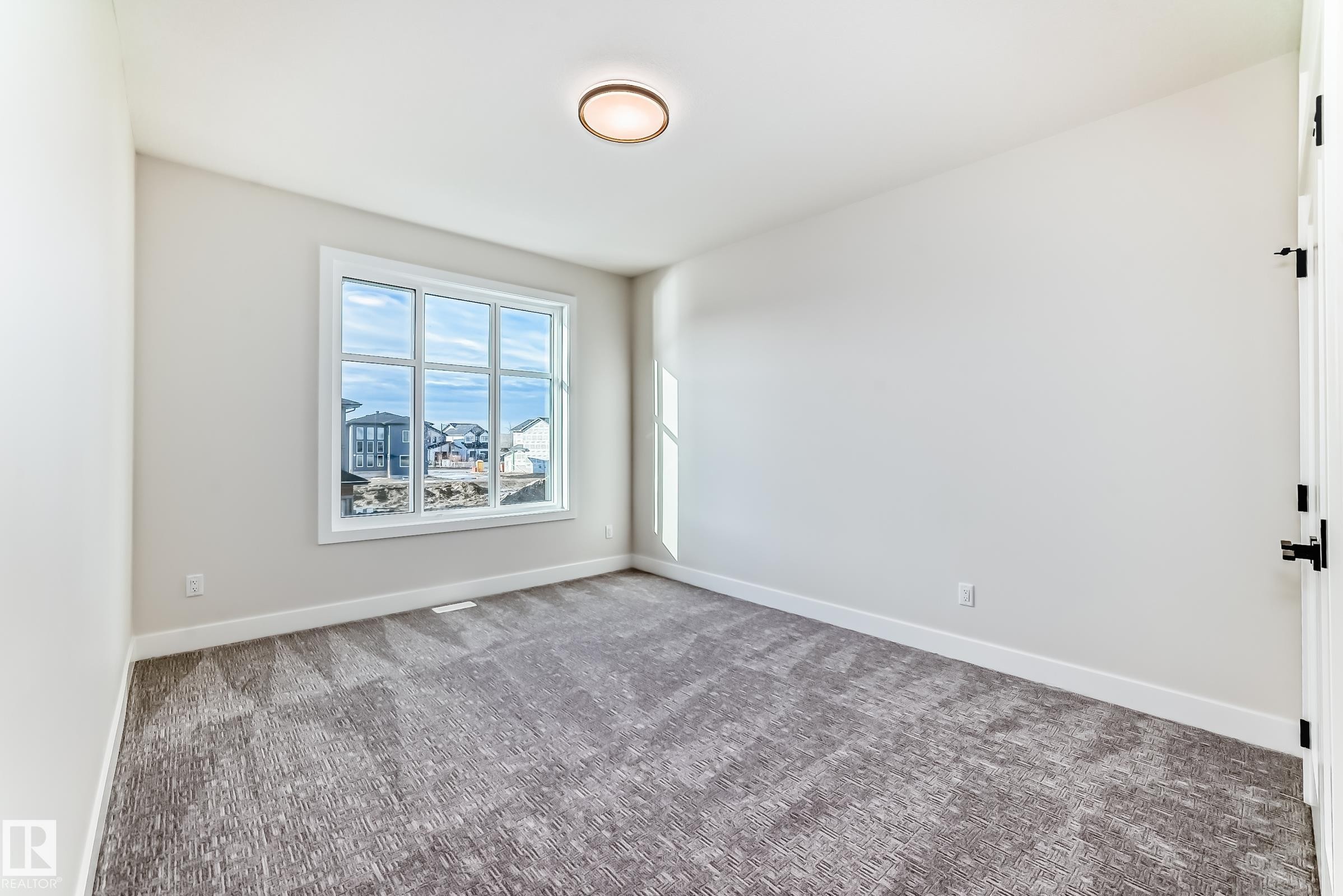 Spacious room featuring light-colored walls, patterned carpeting, and a large window providing natural light - 7665 Kimiwan Crescent, Edmonton, AB - Indoor Photo Showing Other Room