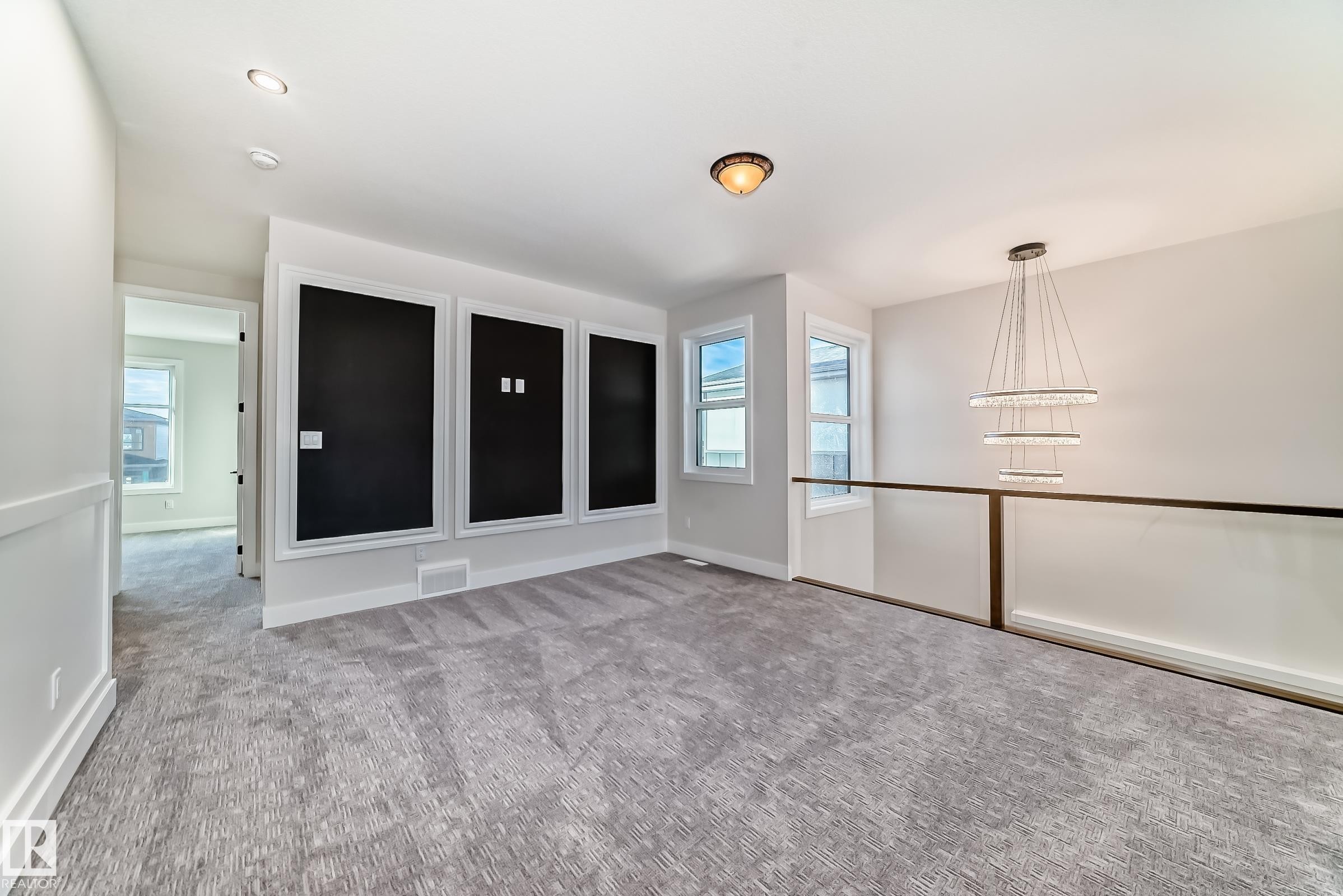 This expansive carpeted room features light-colored walls and a contemporary chandelier - 7665 Kimiwan Crescent, Edmonton, AB - Indoor Photo Showing Other Room