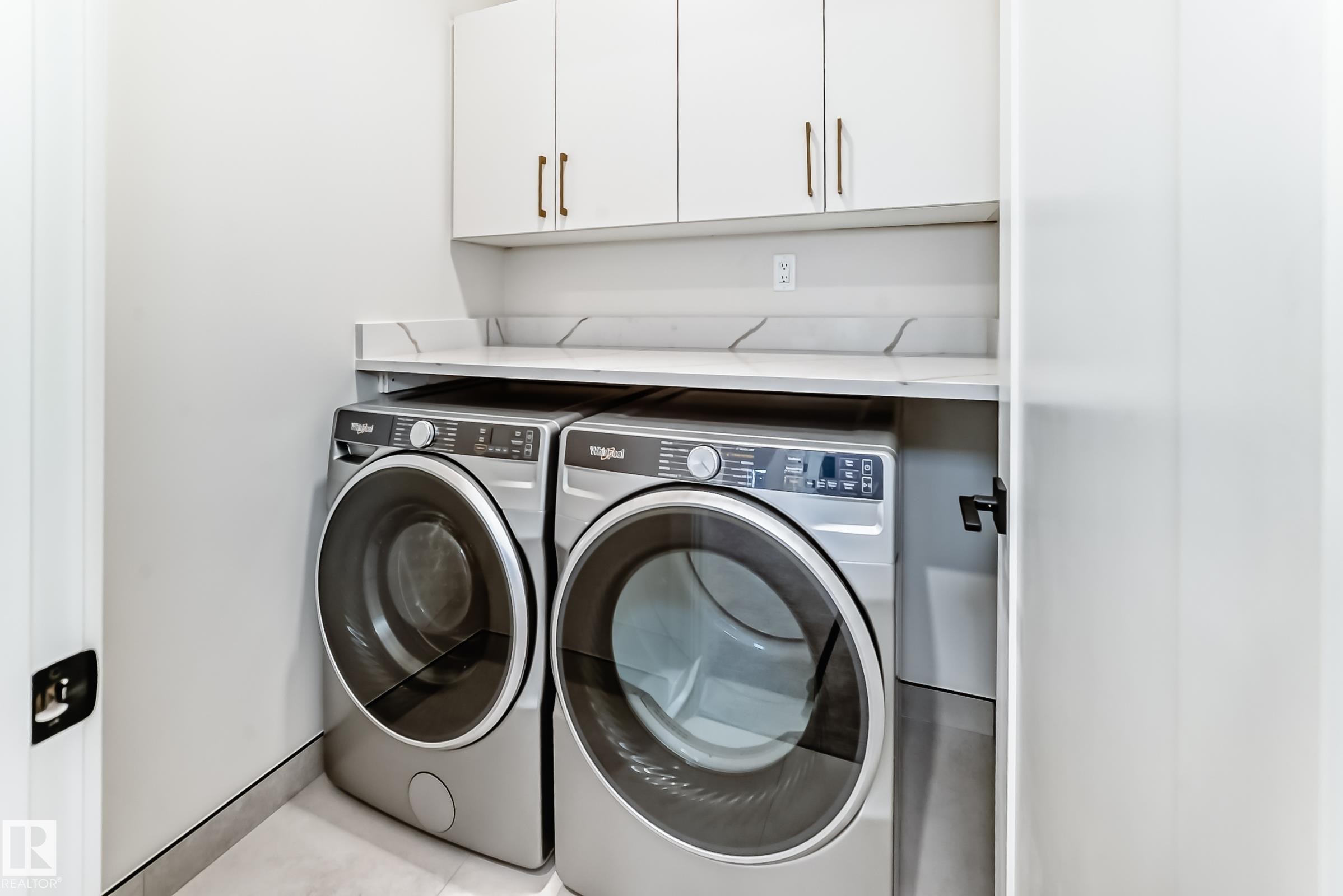 This laundry area features a countertop with a backsplash, white upper cabinetry with brass hardware, and modern appliances - 7665 Kimiwan Crescent, Edmonton, AB - Indoor Photo Showing Laundry Room