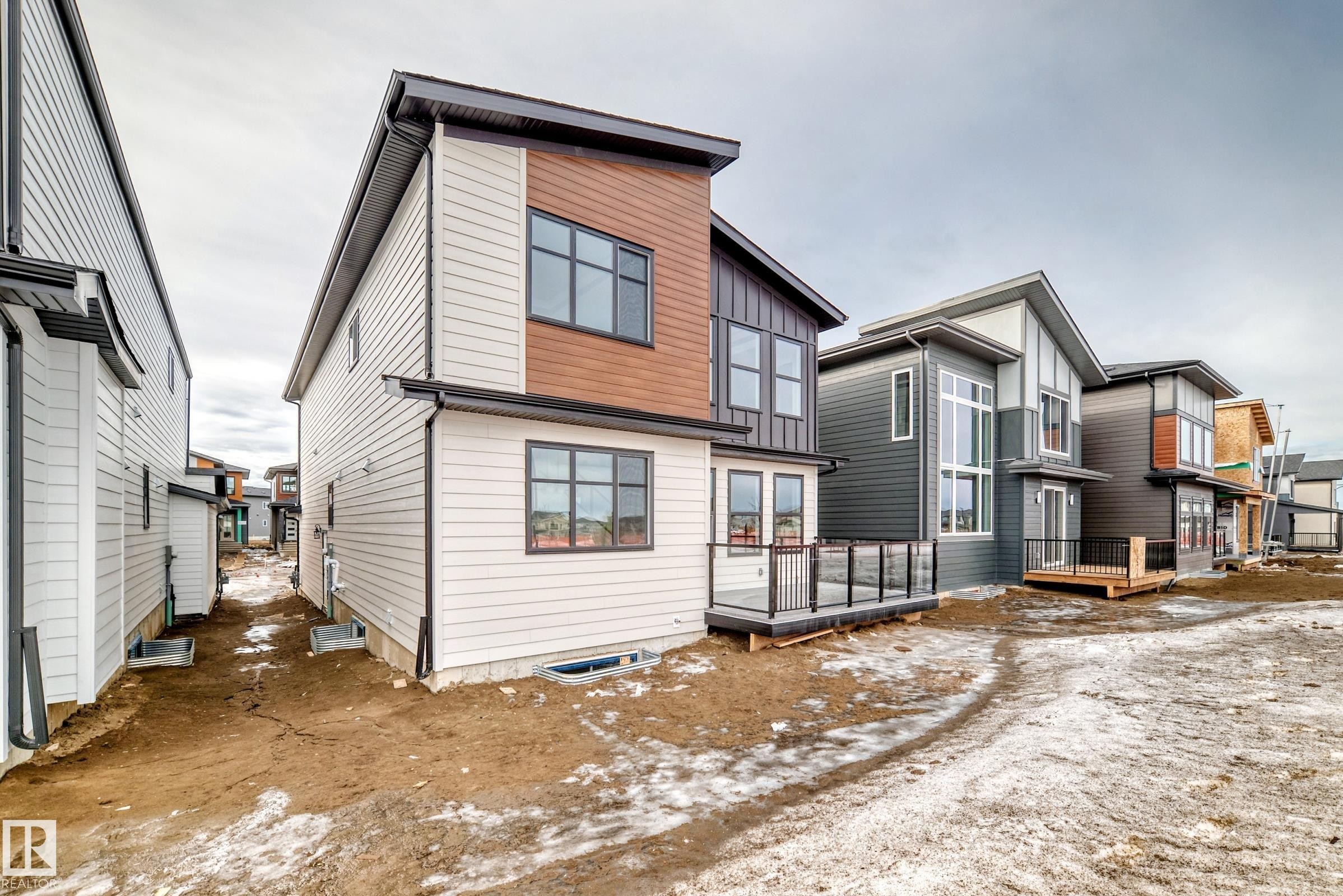 The property features modern architectural design with a blend of light and dark siding, and a deck with dark railings - 7665 Kimiwan Crescent, Edmonton, AB - Outdoor