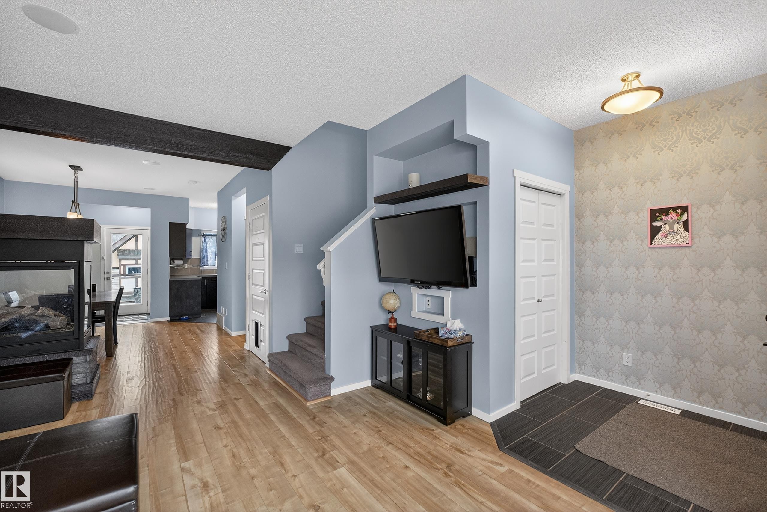 The property features hardwood style flooring, a fireplace with a stone base, a staircase with carpeted treads, and a front entry area with tiled flooring - 1522 Chapman Way, Edmonton, AB - Indoor With Fireplace