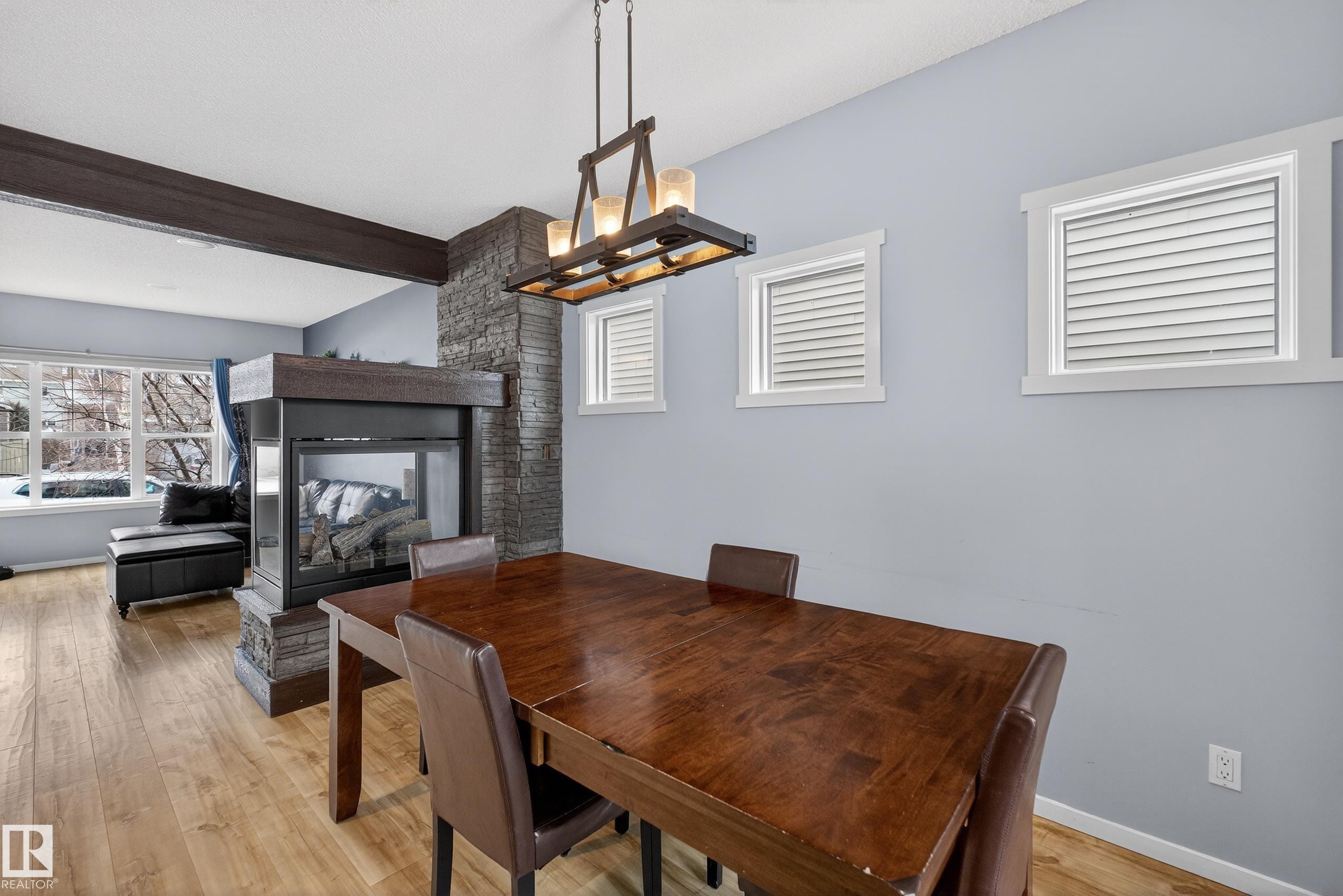 The living area features light hardwood flooring, a stone-clad fireplace, and a large window providing views to the outdoors - 1522 Chapman Way, Edmonton, AB - Indoor Photo Showing Dining Room With Fireplace