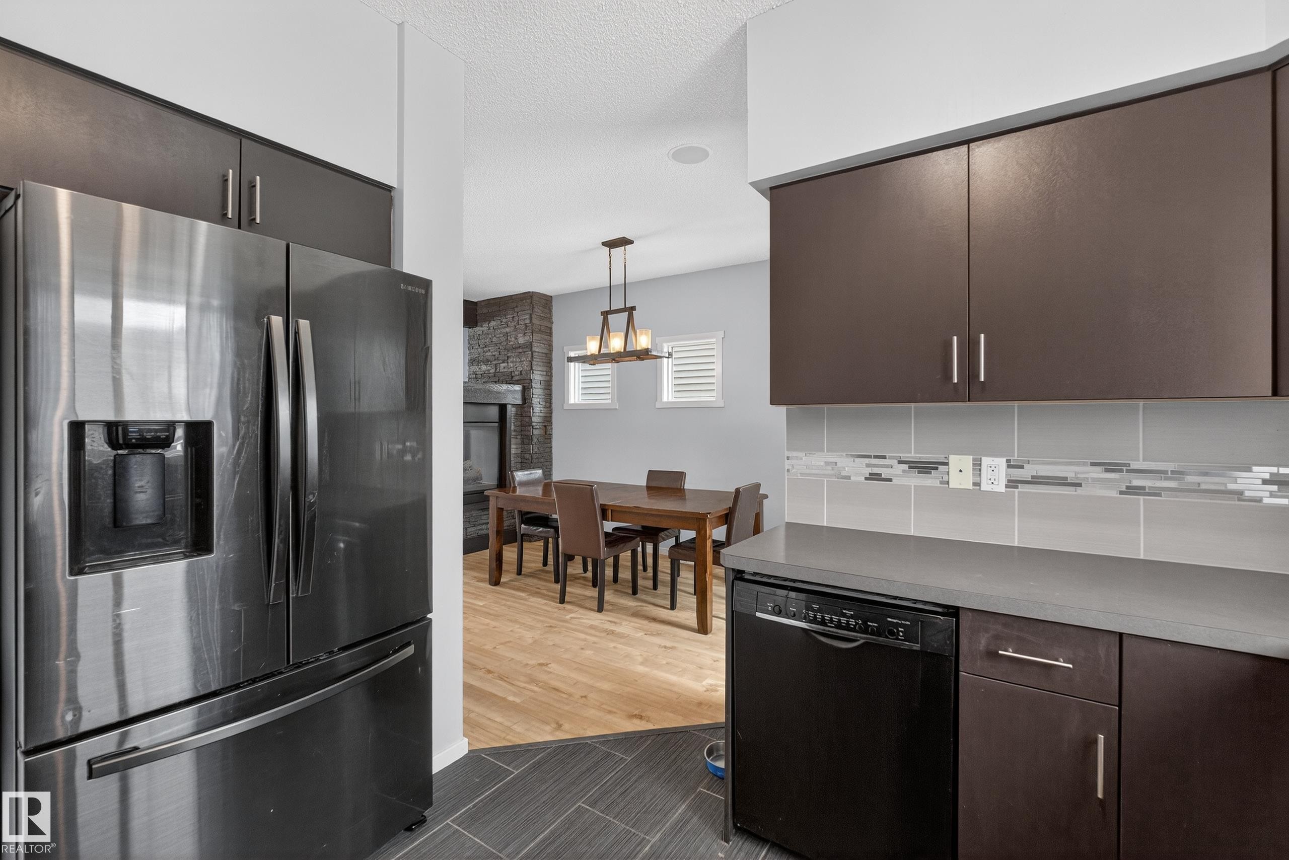 The kitchen features dark wood cabinetry, a stainless steel refrigerator, and a dark dishwasher - 1522 Chapman Way, Edmonton, AB - Indoor Photo Showing Kitchen