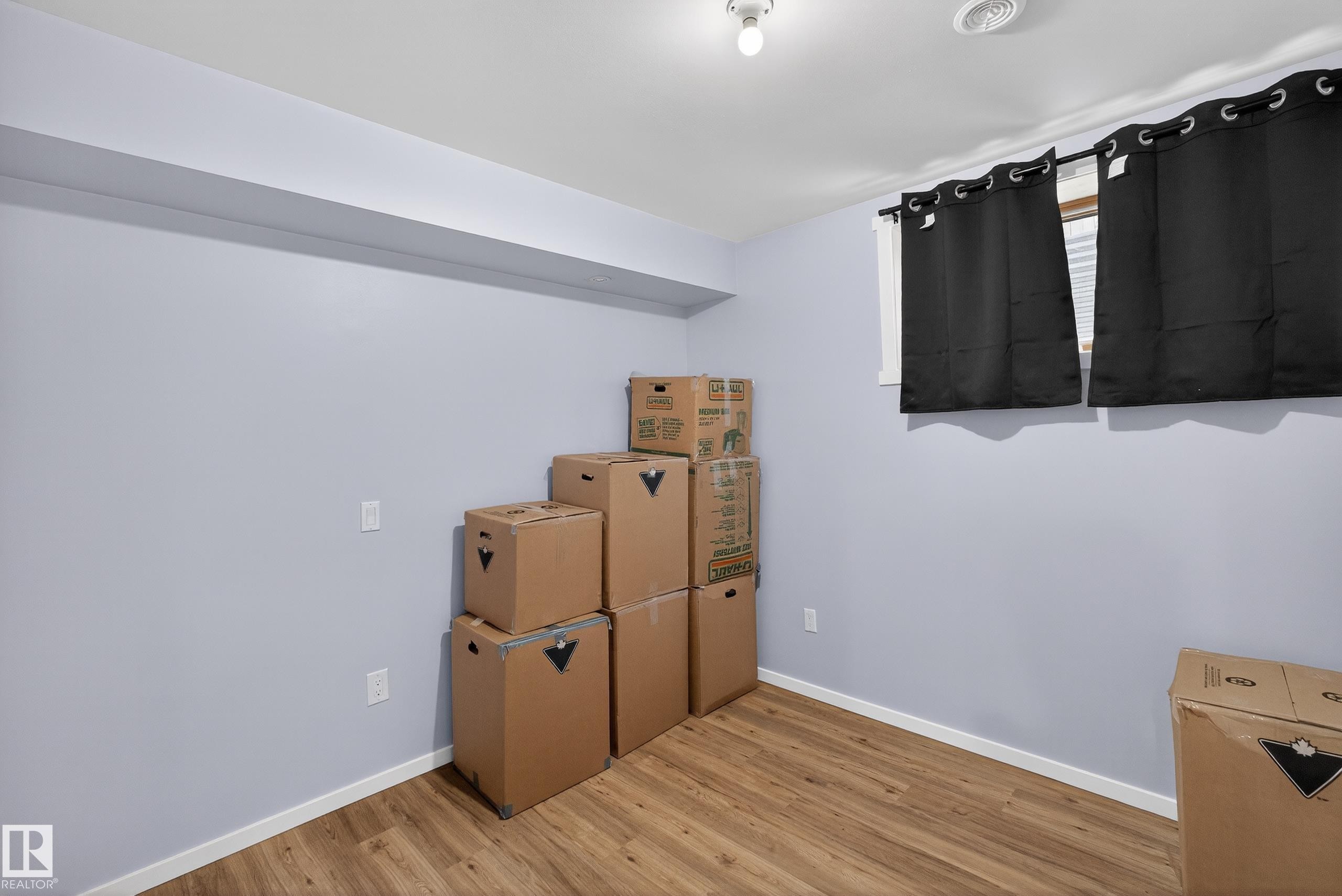 The room features light blue walls, wood-style flooring, and a window with a black curtain - 1522 Chapman Way, Edmonton, AB - Indoor Photo Showing Other Room