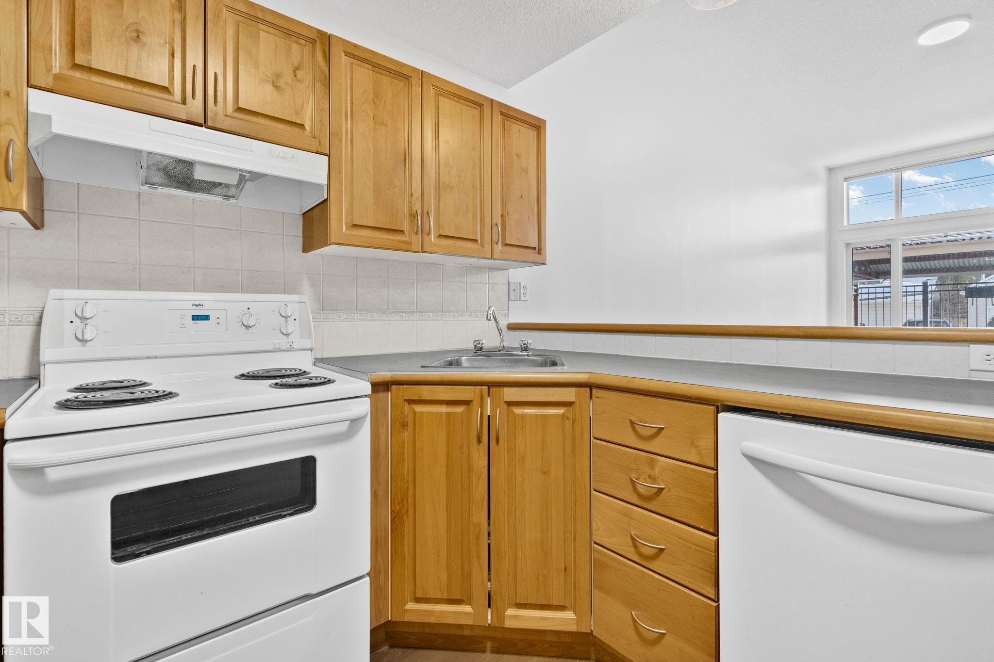 The kitchen features wooden cabinetry, white appliances, and a window providing natural light - 116 11033 127 Street, Edmonton, AB - Indoor Photo Showing Kitchen