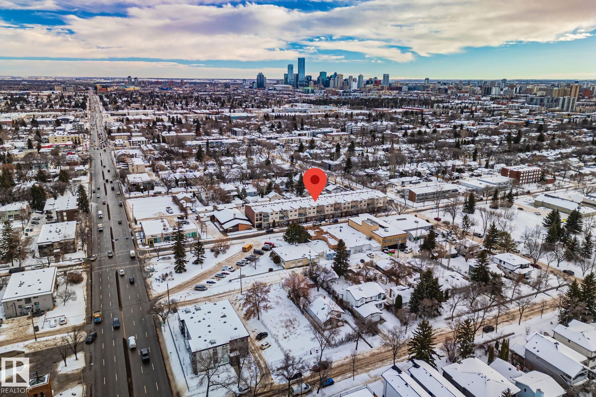 Aerial view showcasing the property's location within a residential area with a prominent roadway and a city skyline visible in the distance - 116 11033 127 Street, Edmonton, AB - Outdoor With View