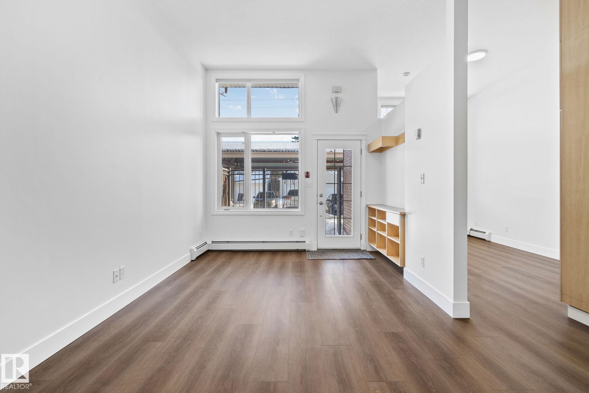 The living space features rich brown flooring and white walls, creating a bright and neutral palette - 116 11033 127 Street, Edmonton, AB - Indoor