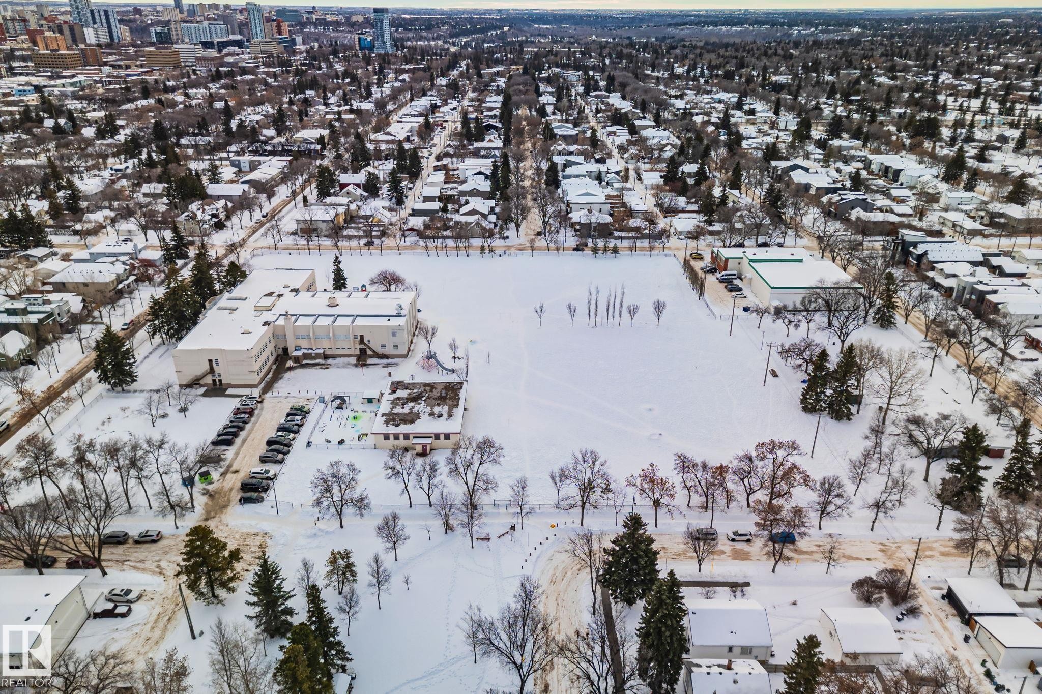 Aerial view of the surrounding neighborhood showcasing residential properties, tree-lined streets, and a large open field, all covered in snow - 116 11033 127 Street, Edmonton, AB - Outdoor With View