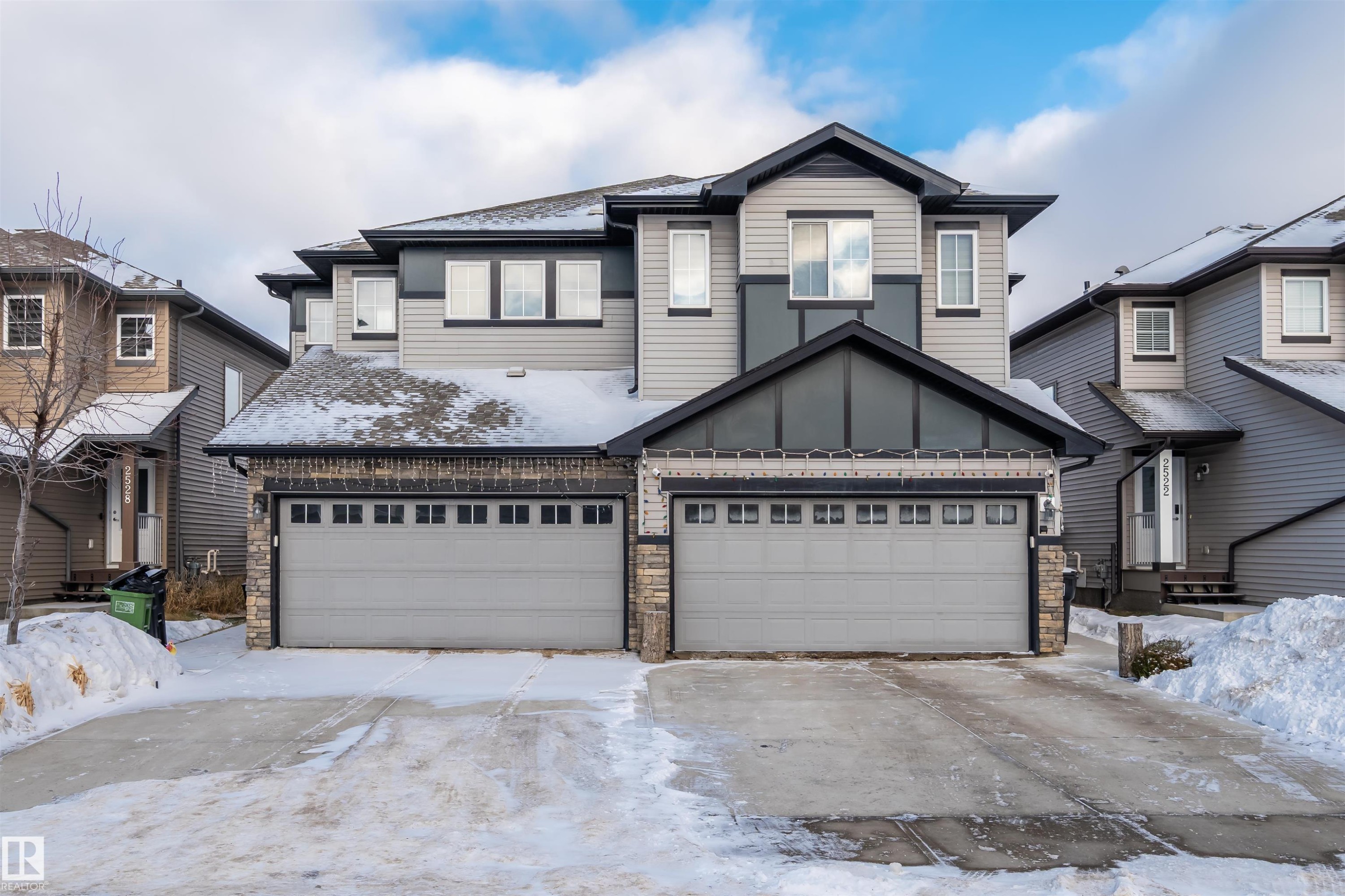 View of front of property with stone siding, concrete driveway, board and batten siding, and an attached garage - 2526 19A Avenue Nw, Edmonton, AB - Outdoor With Facade