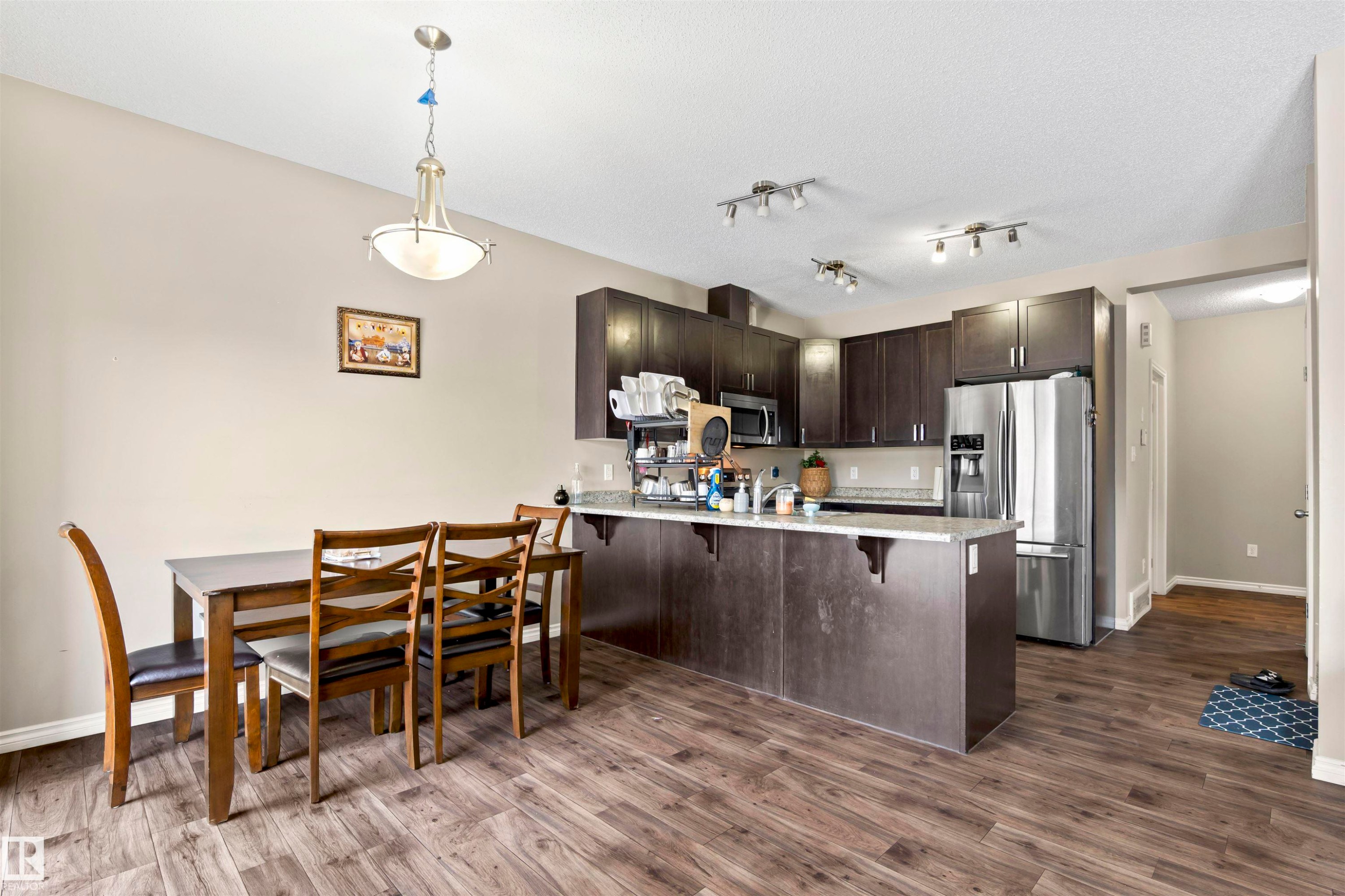 Kitchen with dark brown cabinets, appliances with stainless steel finishes, a peninsula, decorative light fixtures, and a breakfast bar - 2526 19A Avenue Nw, Edmonton, AB - Indoor