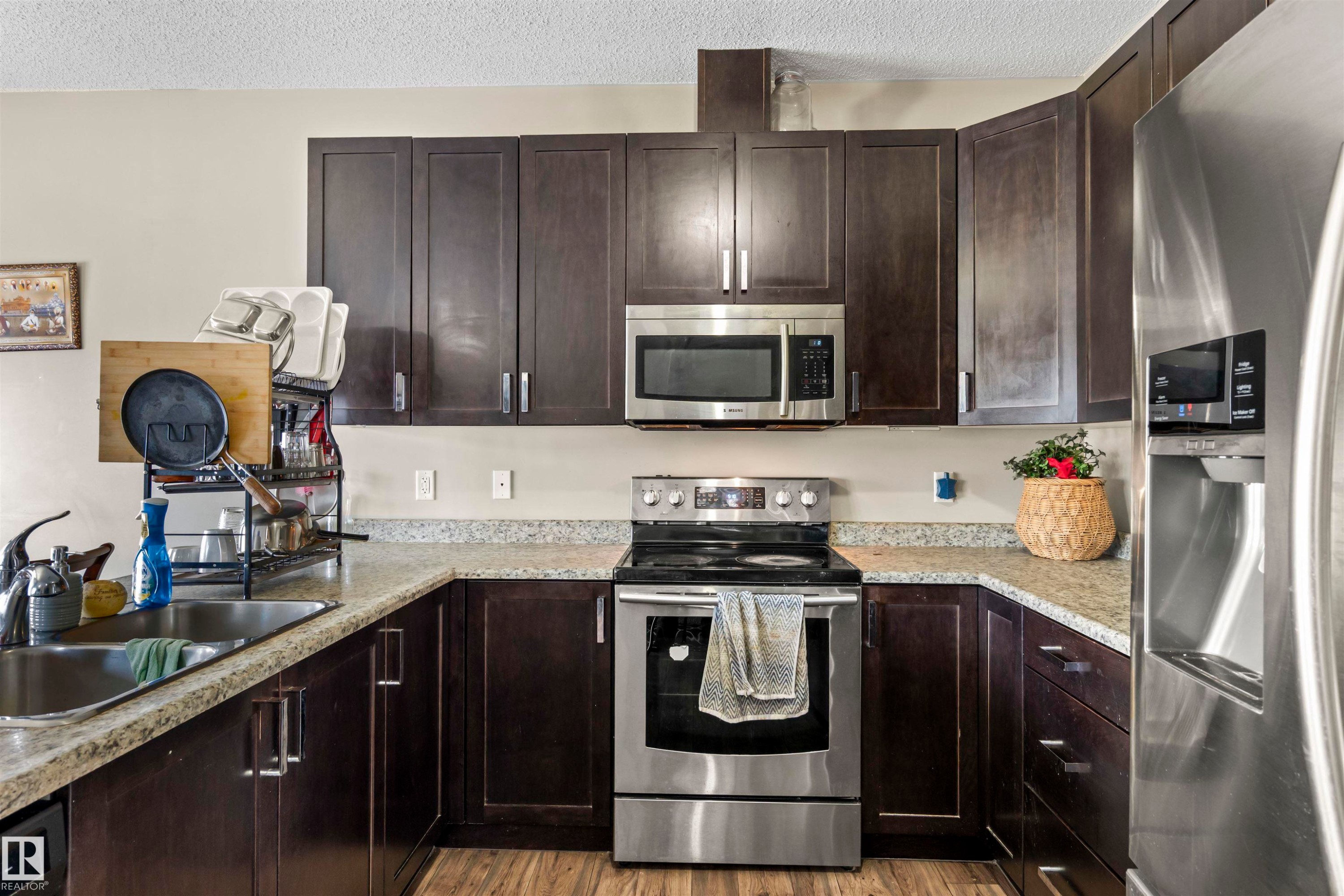 Kitchen featuring appliances with stainless steel finishes, dark brown cabinetry, a textured ceiling, and light wood finished floors - 2526 19A Avenue Nw, Edmonton, AB - Indoor Photo Showing Kitchen With Stainless Steel Kitchen With Double Sink With Upgraded Kitchen