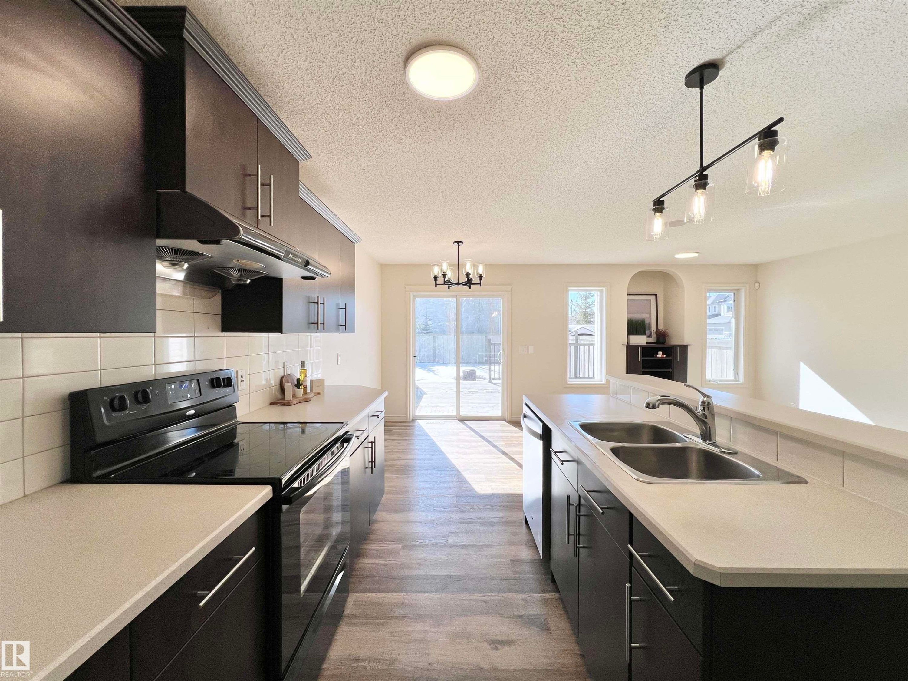 The kitchen features dark cabinetry, white countertops, a double basin sink, and black appliances - 17127 7A Avenue, Edmonton, AB - Indoor Photo Showing Kitchen With Double Sink