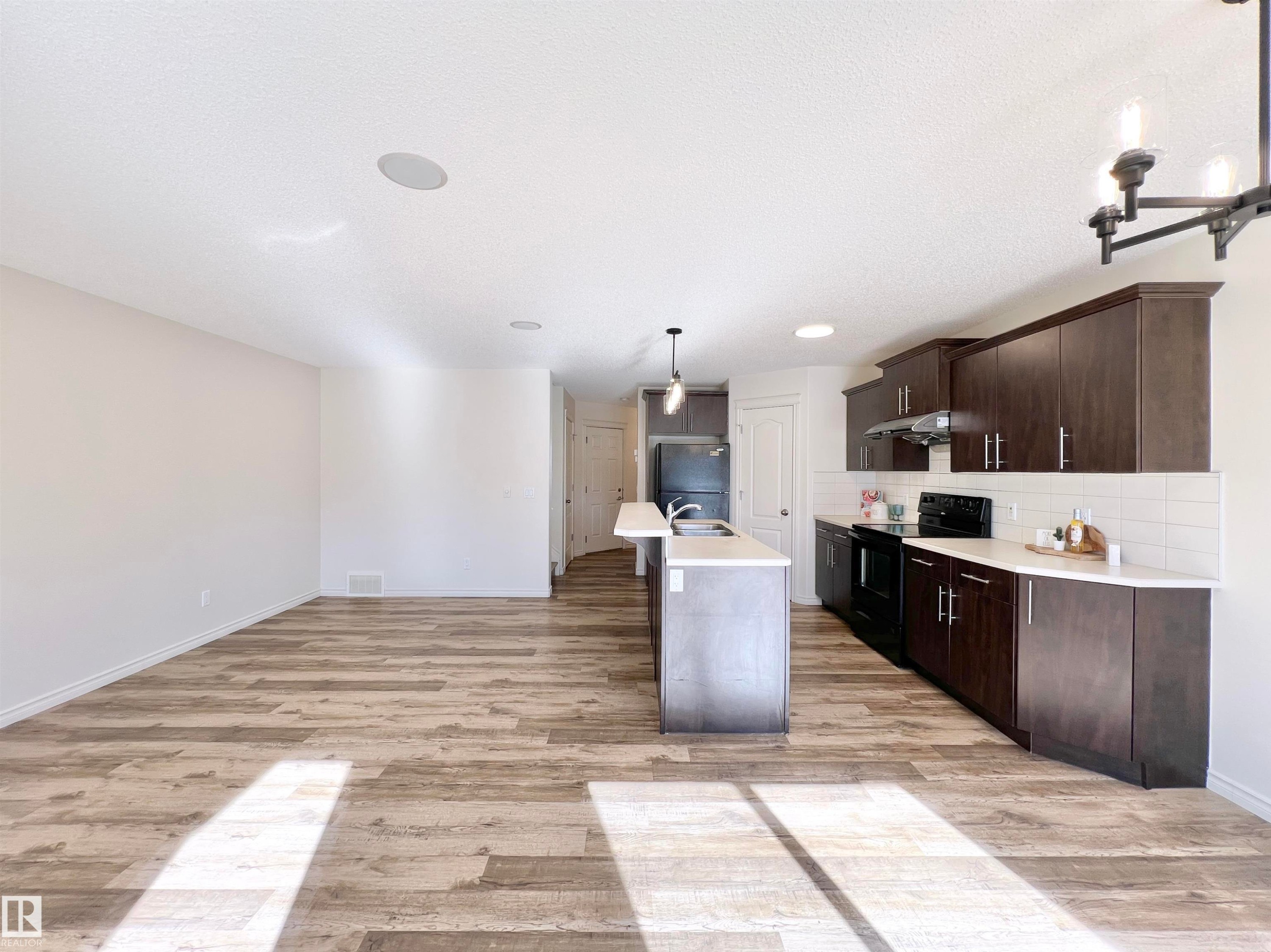 Open concept living area featuring wood-look flooring, a kitchen island with sink, dark wood cabinetry, and a white subway tile backsplash - 17127 7A Avenue, Edmonton, AB - Indoor Photo Showing Kitchen