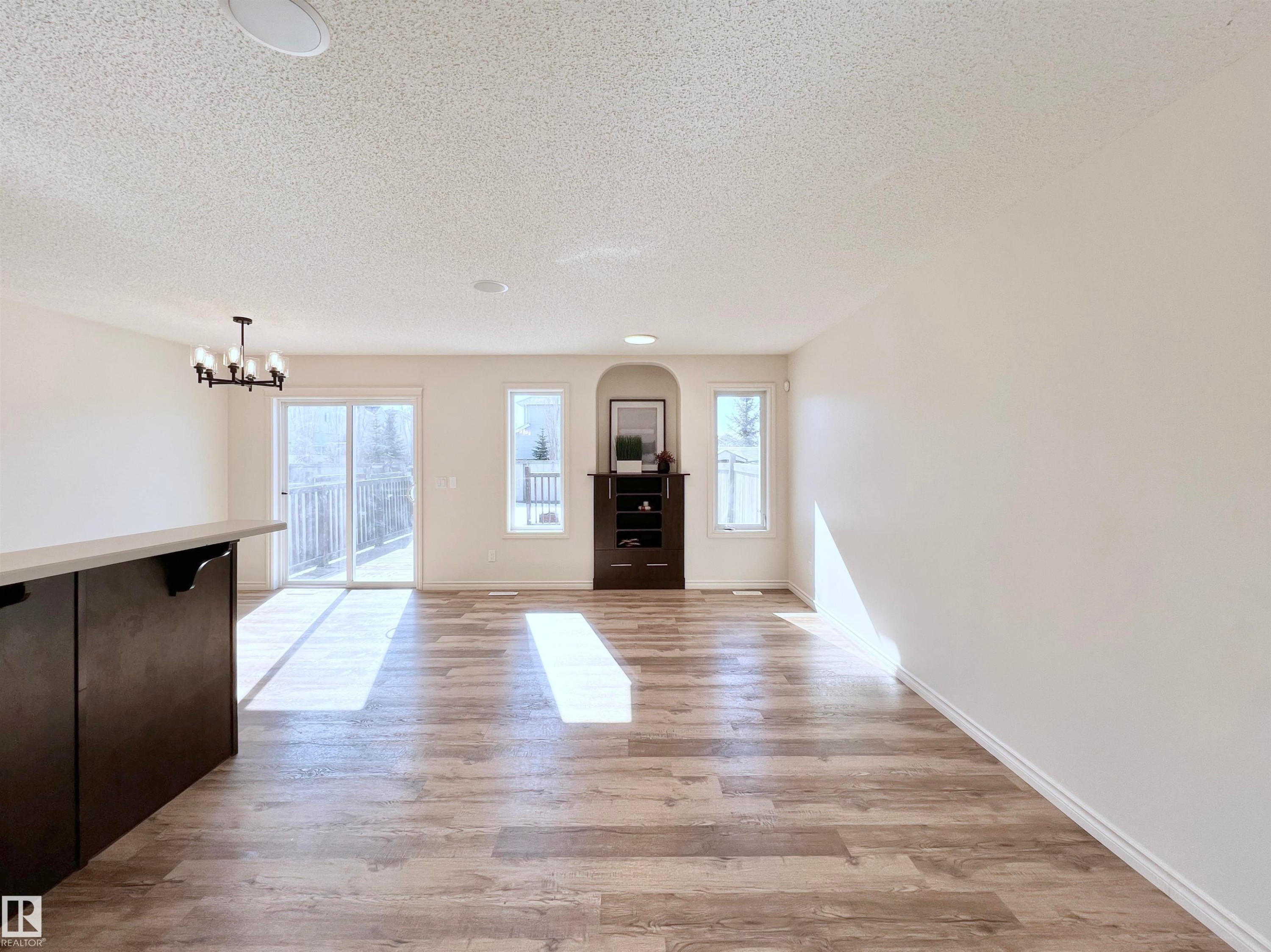 Expansive living area featuring wood-look flooring, white walls, and a sliding glass door leading to an outdoor space - 17127 7A Avenue, Edmonton, AB - Indoor