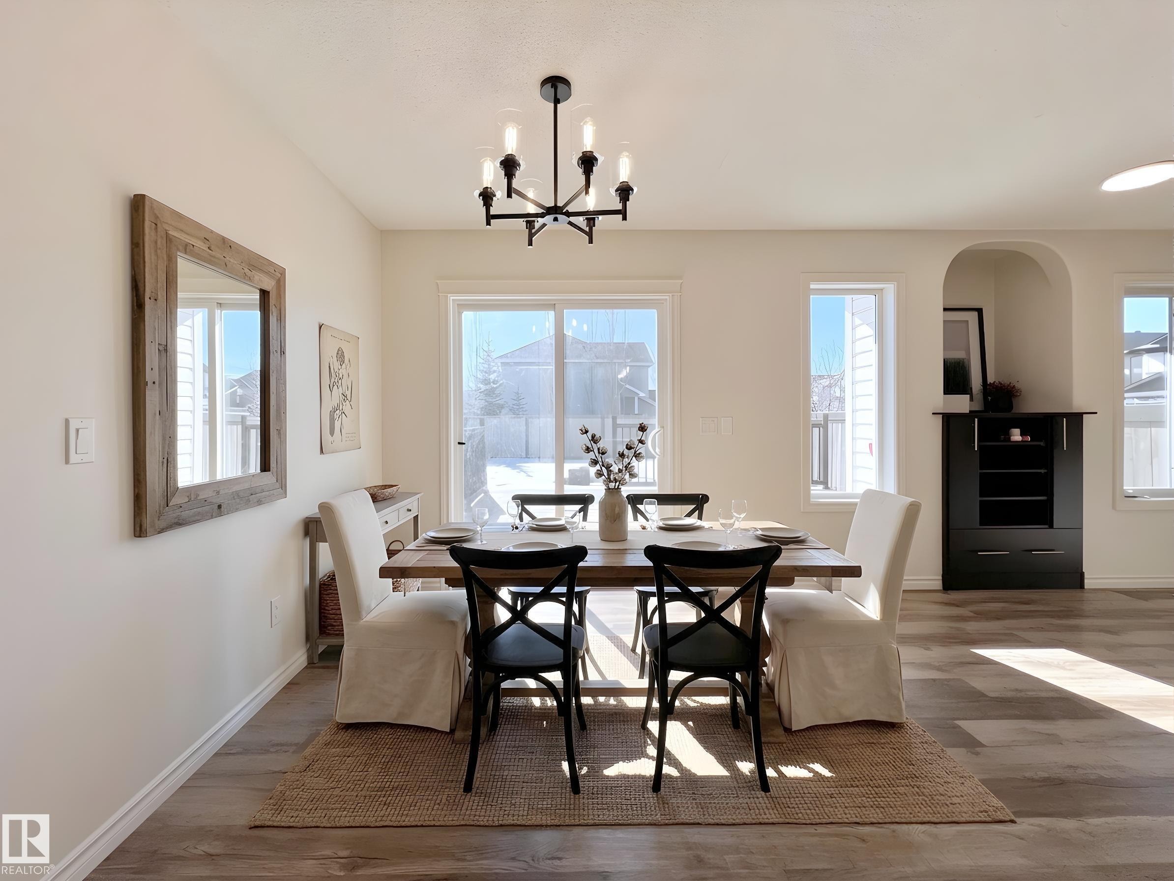 This dining area features light-colored walls, a sliding glass door, and a modern chandelier - 17127 7A Avenue, Edmonton, AB - Indoor Photo Showing Dining Room