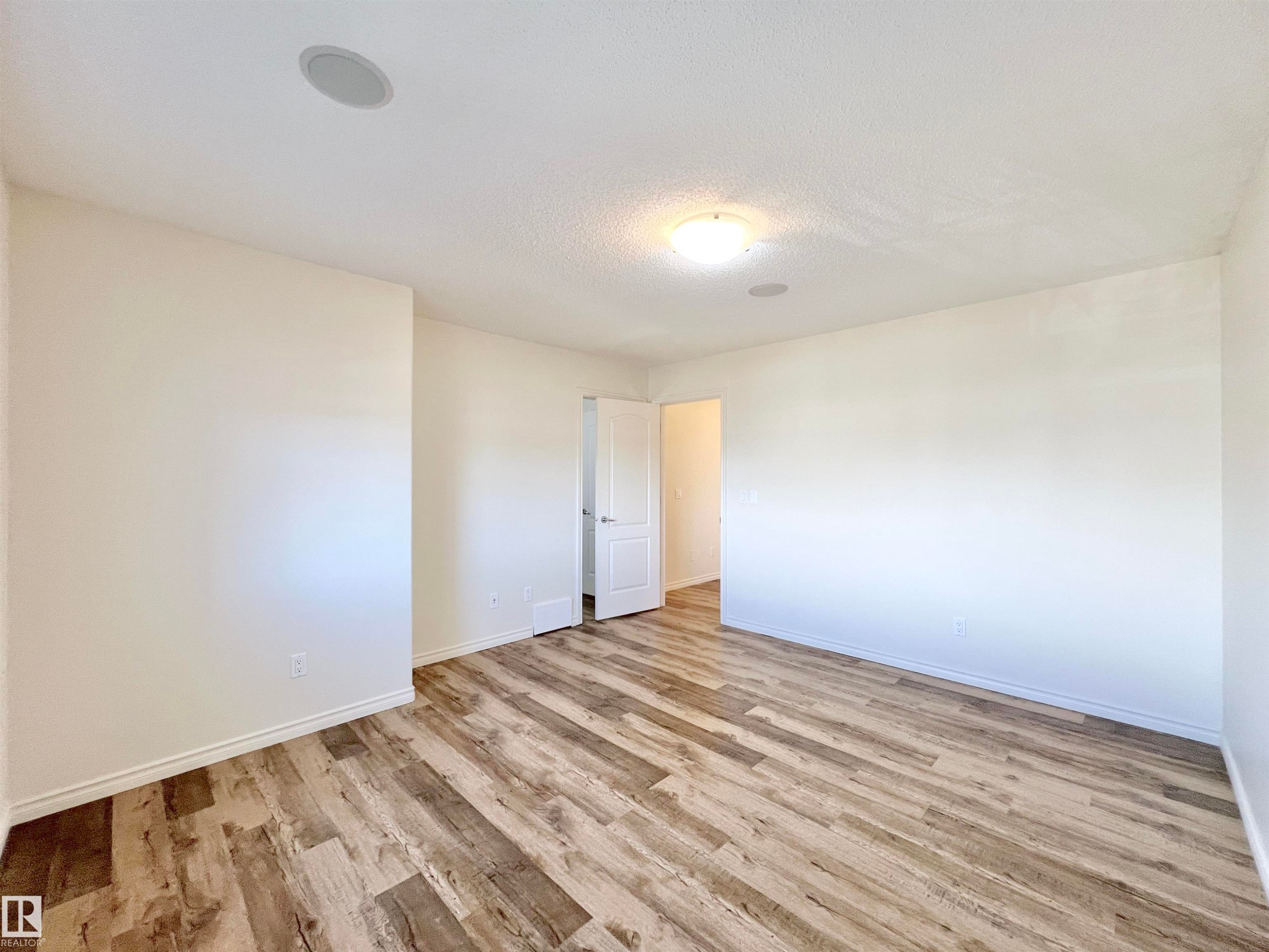 This spacious room features light-colored walls and wood-style flooring, creating a bright and inviting atmosphere - 17127 7A Avenue, Edmonton, AB - Indoor Photo Showing Other Room