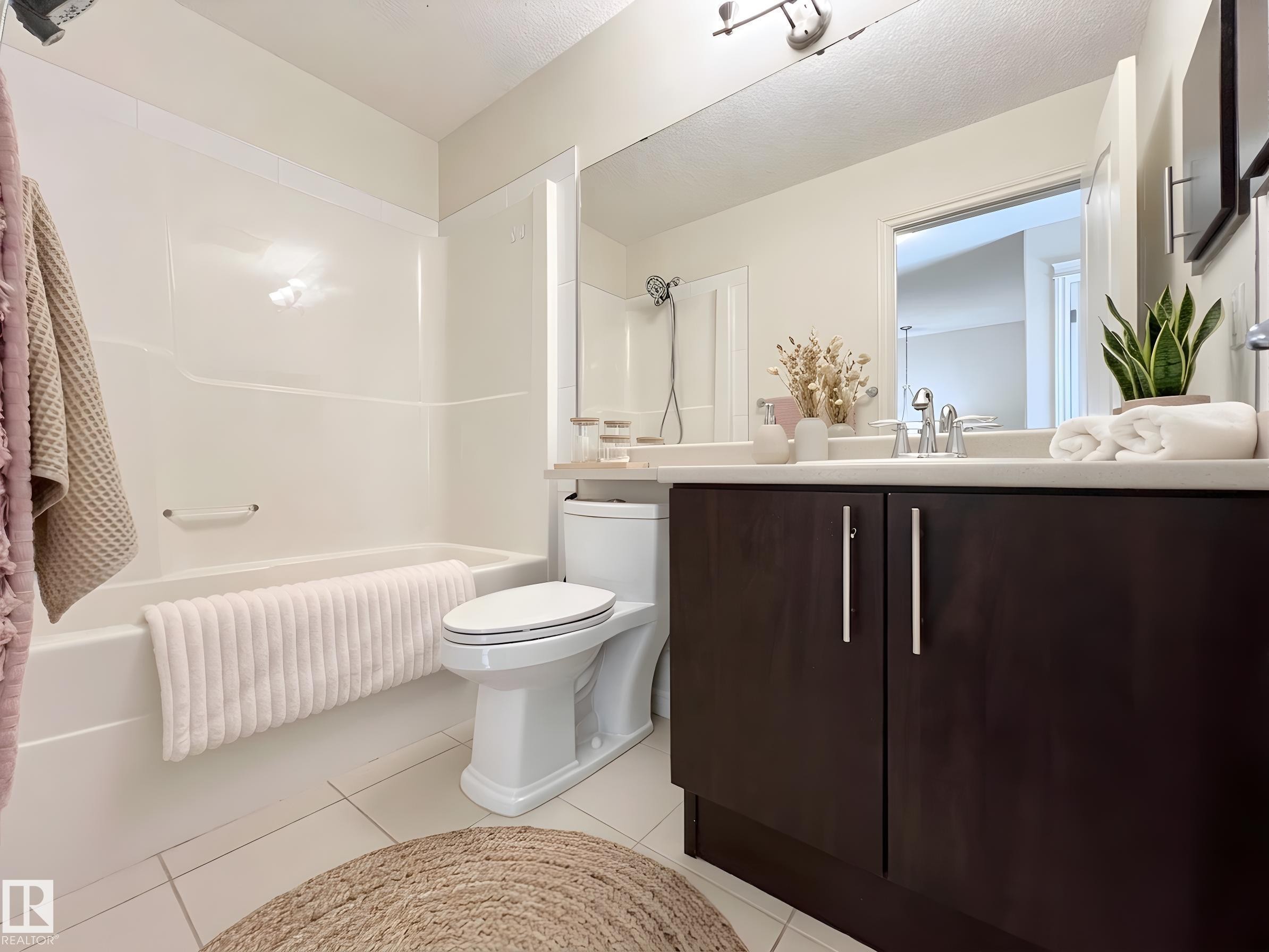 Bathroom featuring a white bathtub and shower combination, a toilet, a vanity with a dark wood finish and silver hardware, and a large wall-mounted mirror - 17127 7A Avenue, Edmonton, AB - Indoor Photo Showing Bathroom