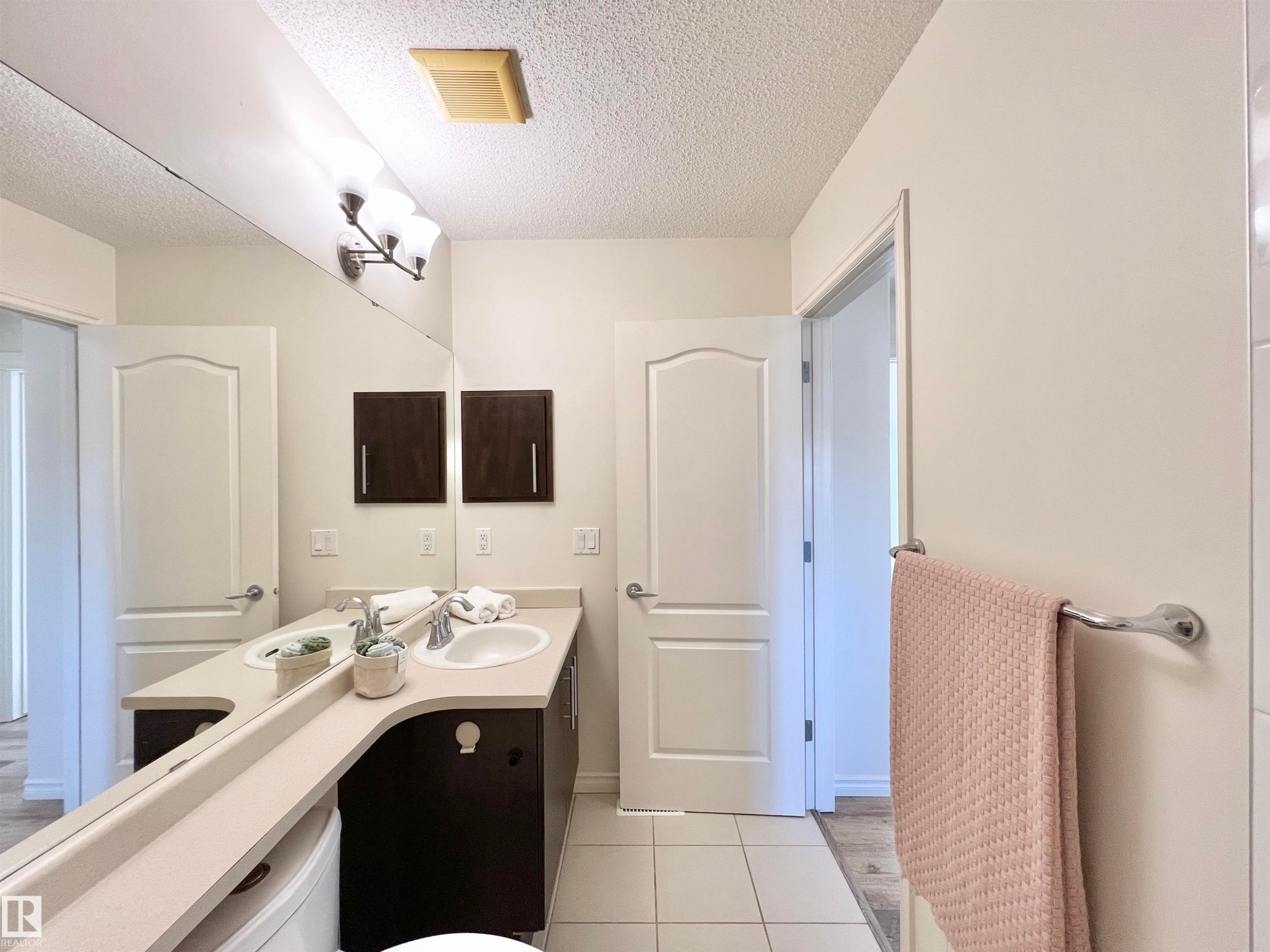 Bathroom featuring a dual sink vanity with dark wood cabinetry, light-colored countertops, and a large mirror - 17127 7A Avenue, Edmonton, AB - Indoor