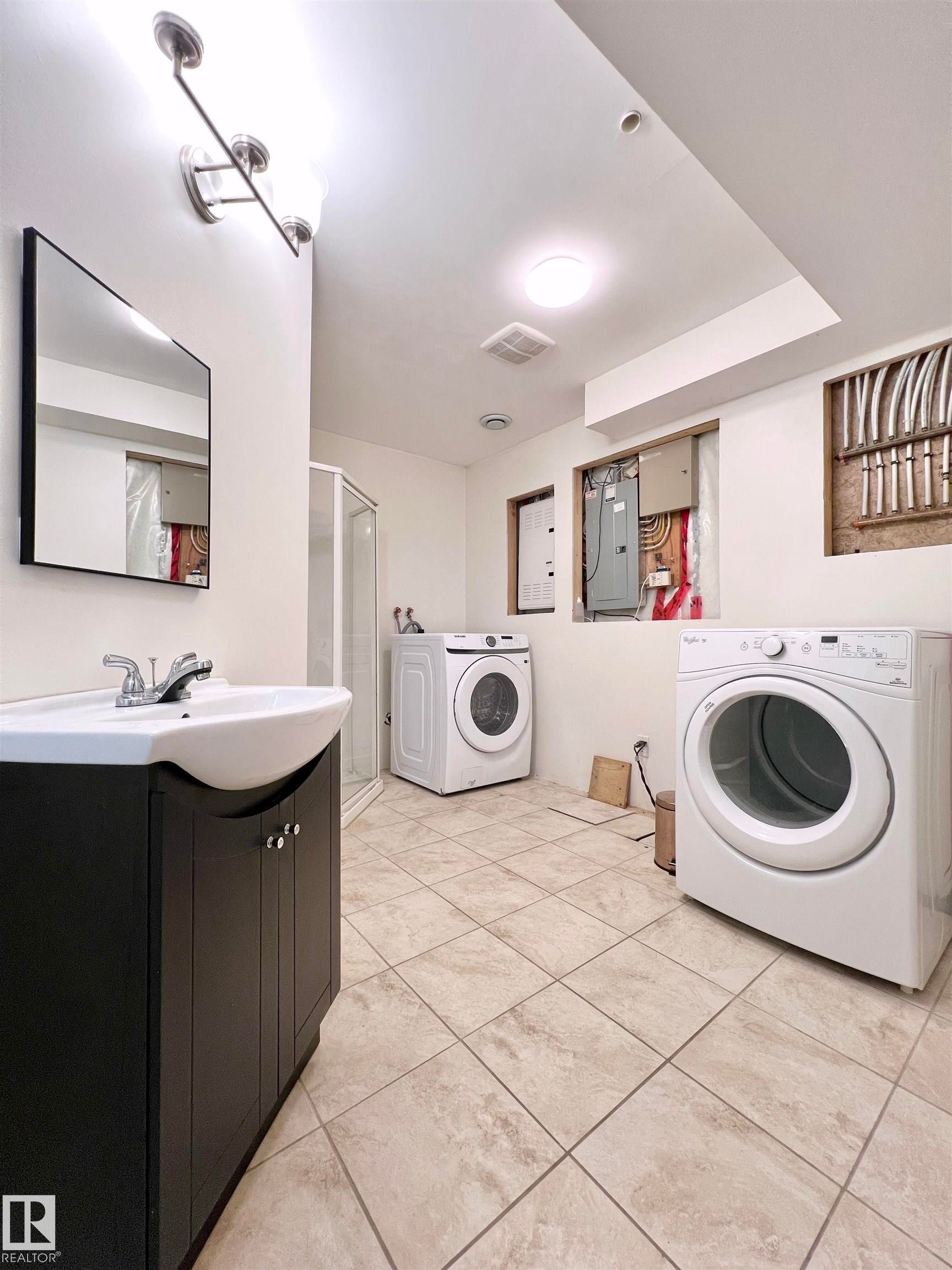 Spacious utility area featuring a dark wood vanity with a white sink, a mirror, and tiled flooring - 17127 7A Avenue, Edmonton, AB - Indoor Photo Showing Laundry Room
