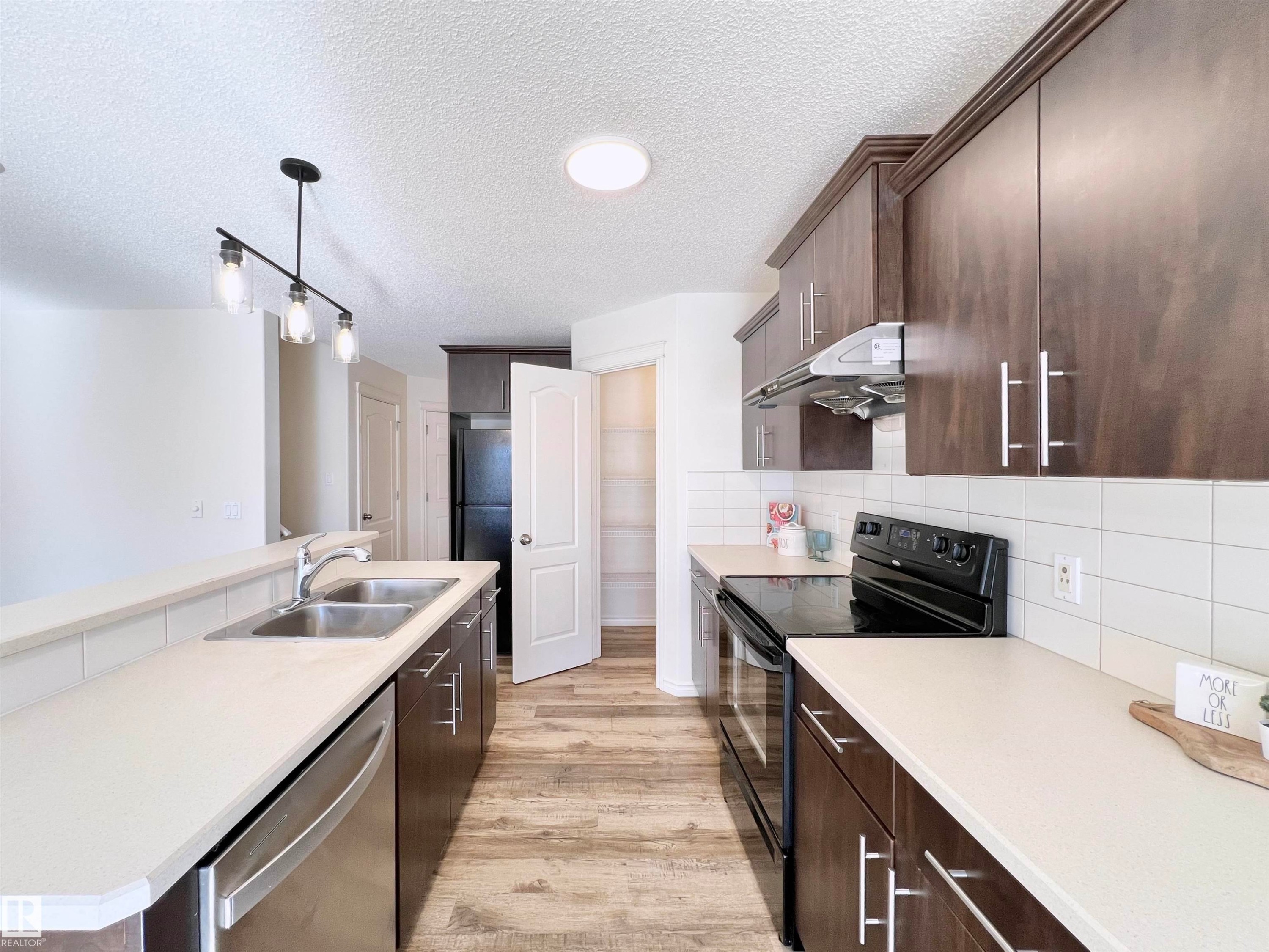 The kitchen features dark wood cabinetry, light countertops, and a white subway tile backsplash - 17127 7A Avenue, Edmonton, AB - Indoor Photo Showing Kitchen With Double Sink