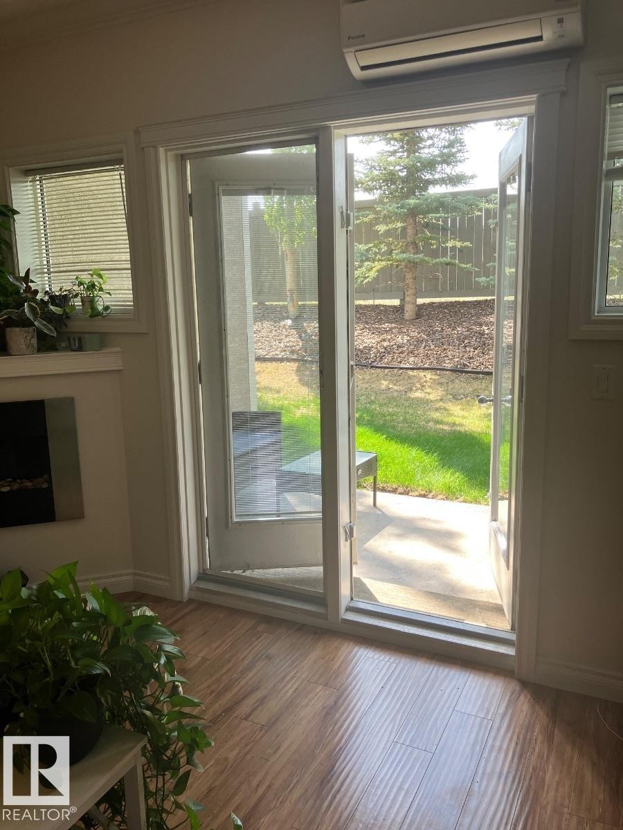 The property features hardwood floors, a wall-mounted air conditioning unit, and a glass paneled door that opens to an outdoor patio area with a fenced yard - 145 10121 80 Avenue, Edmonton, AB - Indoor Photo Showing Other Room