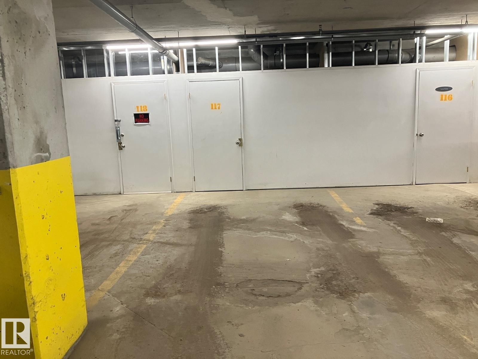 The property offers dedicated storage units with white doors and visible numbering, alongside marked parking spaces on a concrete floor - 145 10121 80 Avenue, Edmonton, AB - Indoor Photo Showing Garage