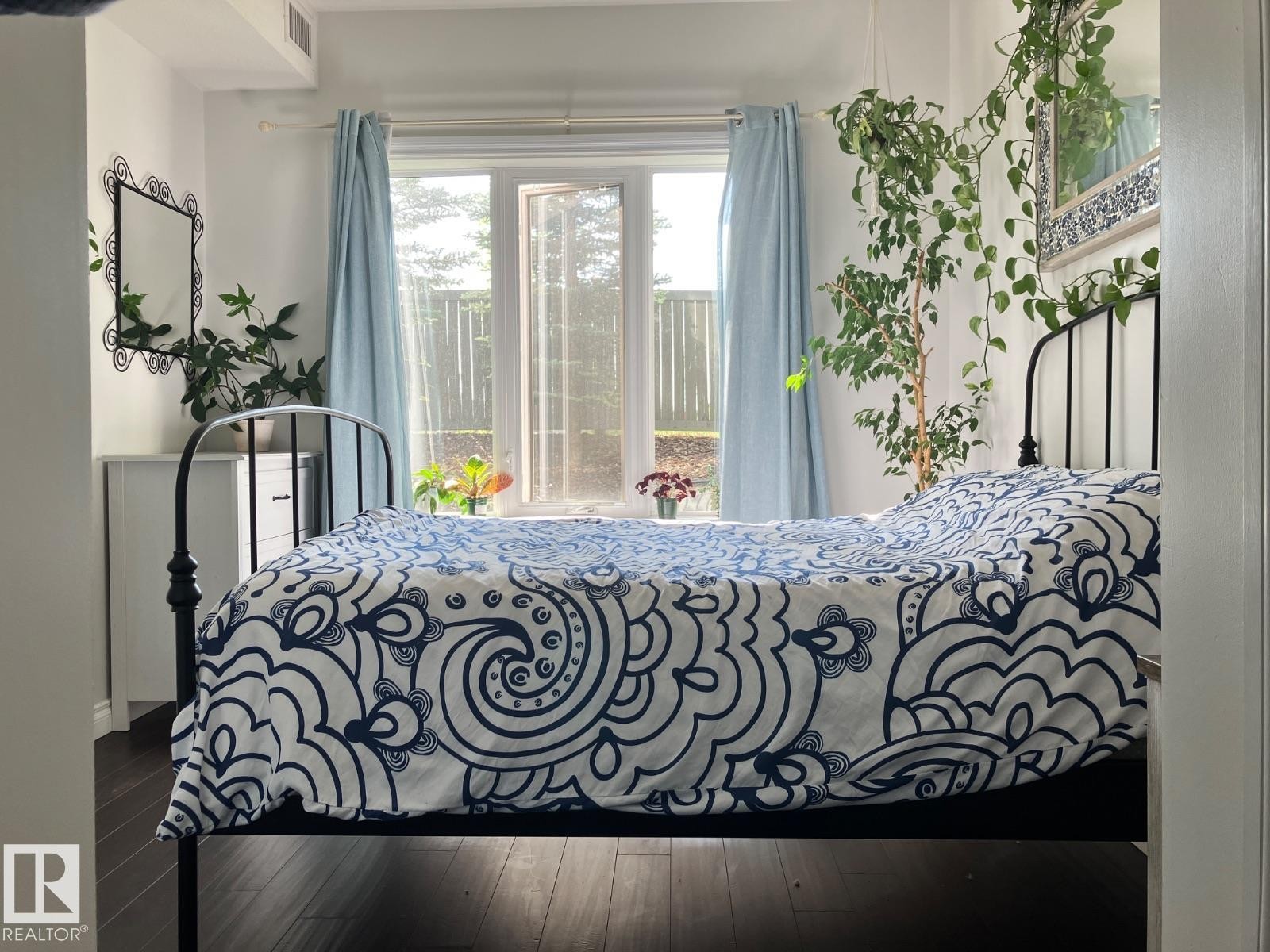 This room features dark hardwood flooring and a window with light blue curtains - 145 10121 80 Avenue, Edmonton, AB - Indoor Photo Showing Bedroom