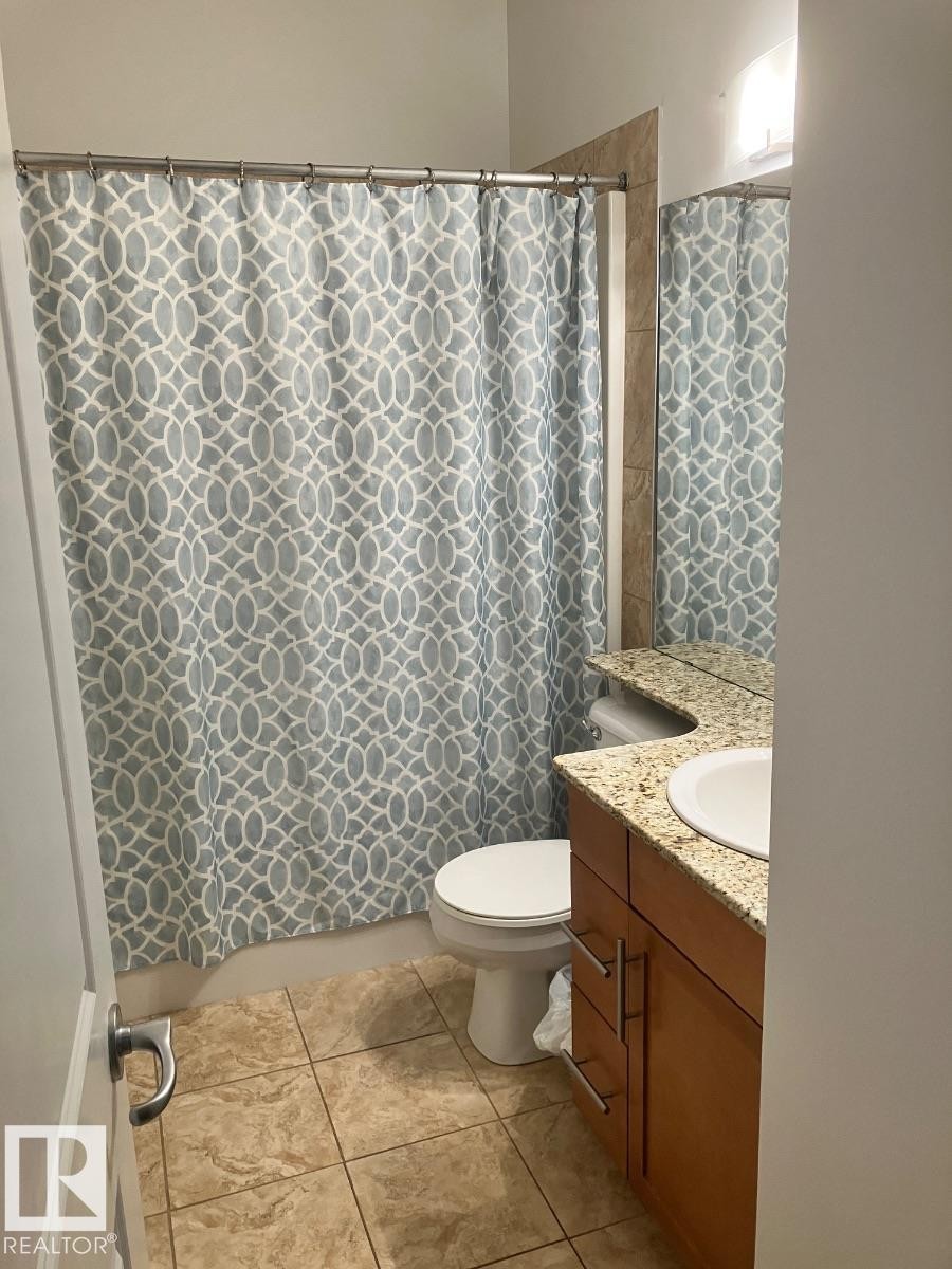 Bathroom featuring tiled flooring, a toilet, and a vanity with a granite countertop and an integrated sink - 145 10121 80 Avenue, Edmonton, AB - Indoor Photo Showing Bathroom