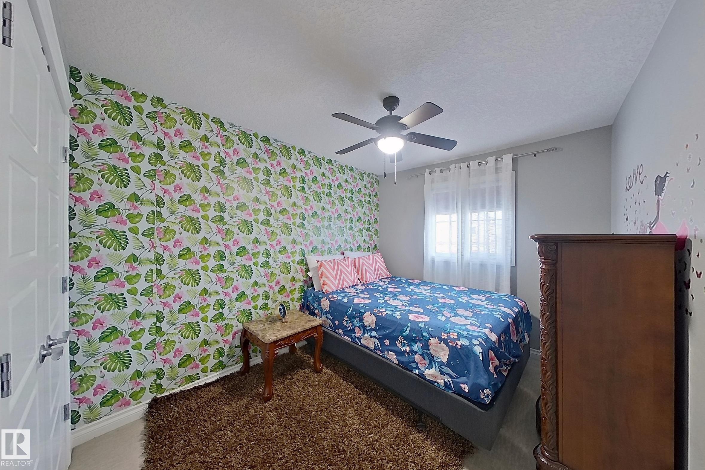 This room features a distinct accent wall with a botanical pattern, a ceiling fan with integrated lighting, and a window with sheer curtains - 1743 60 Street Sw, Edmonton, AB - Indoor Photo Showing Bedroom