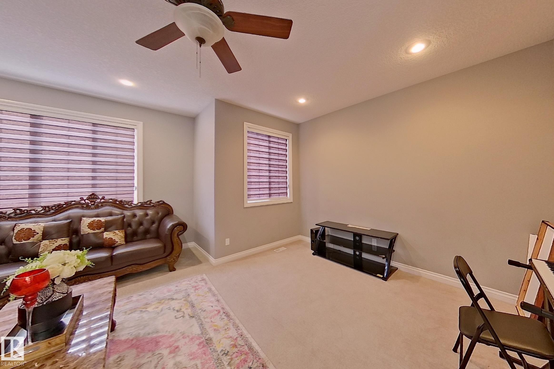This living space features light-colored carpeting, two windows with horizontal blinds, and recessed lighting in the ceiling - 1743 60 Street Sw, Edmonton, AB - Indoor