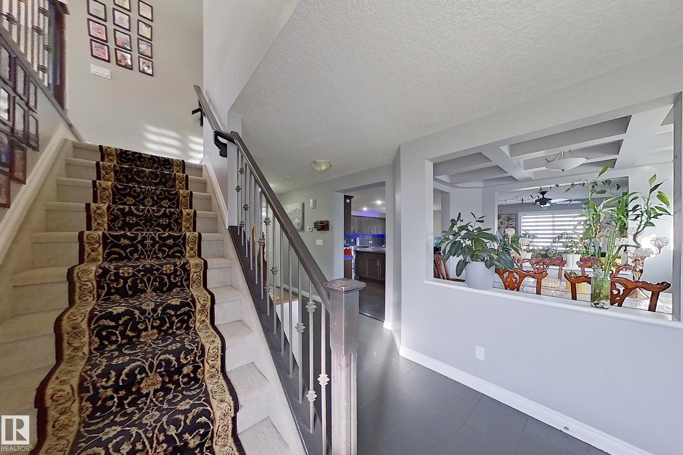 The property features a staircase with a patterned runner, and a half-wall opening that provides a view into an adjacent area with a coffered ceiling - 1743 60 Street Sw, Edmonton, AB - Indoor Photo Showing Other Room